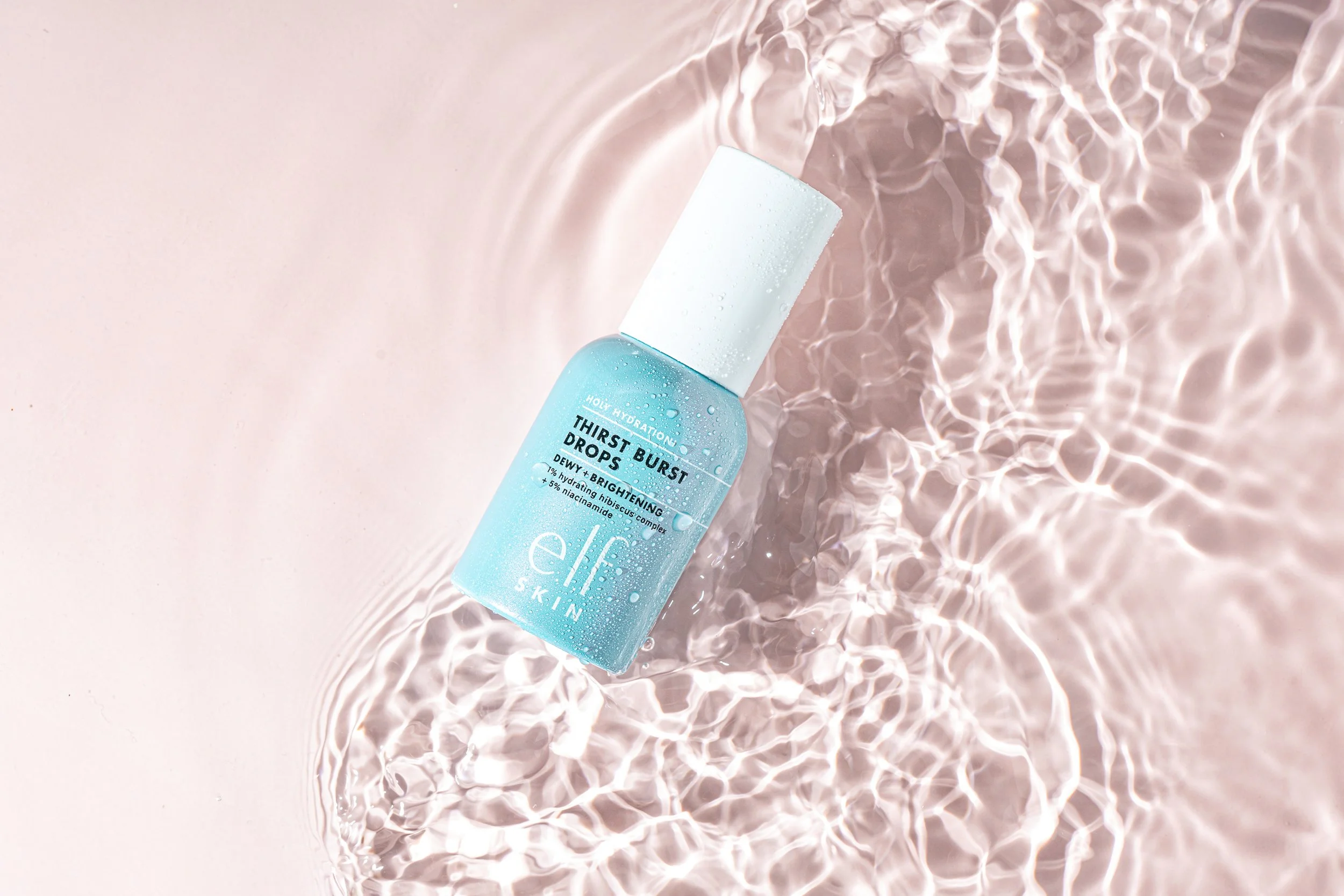 A bottle of e.l.f. skincare Thirst Burst Drops submerged in water with rippling reflections and light pattern on the water's surface.