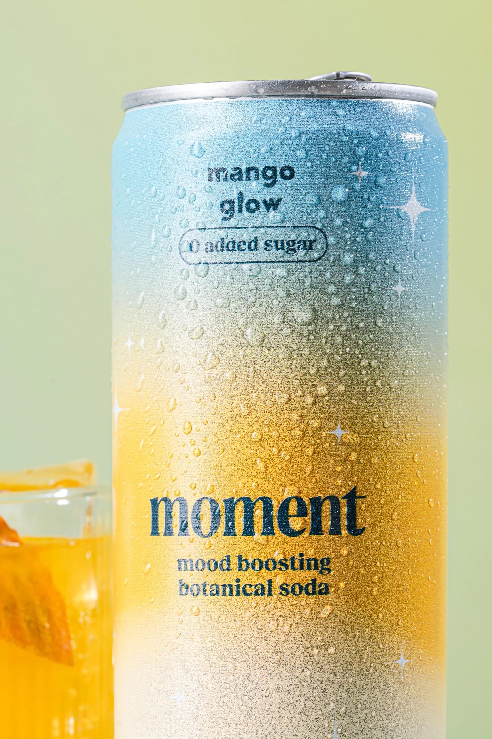 Close-up of a can of Mango Glow botanical soda with droplets of condensation on the surface.
