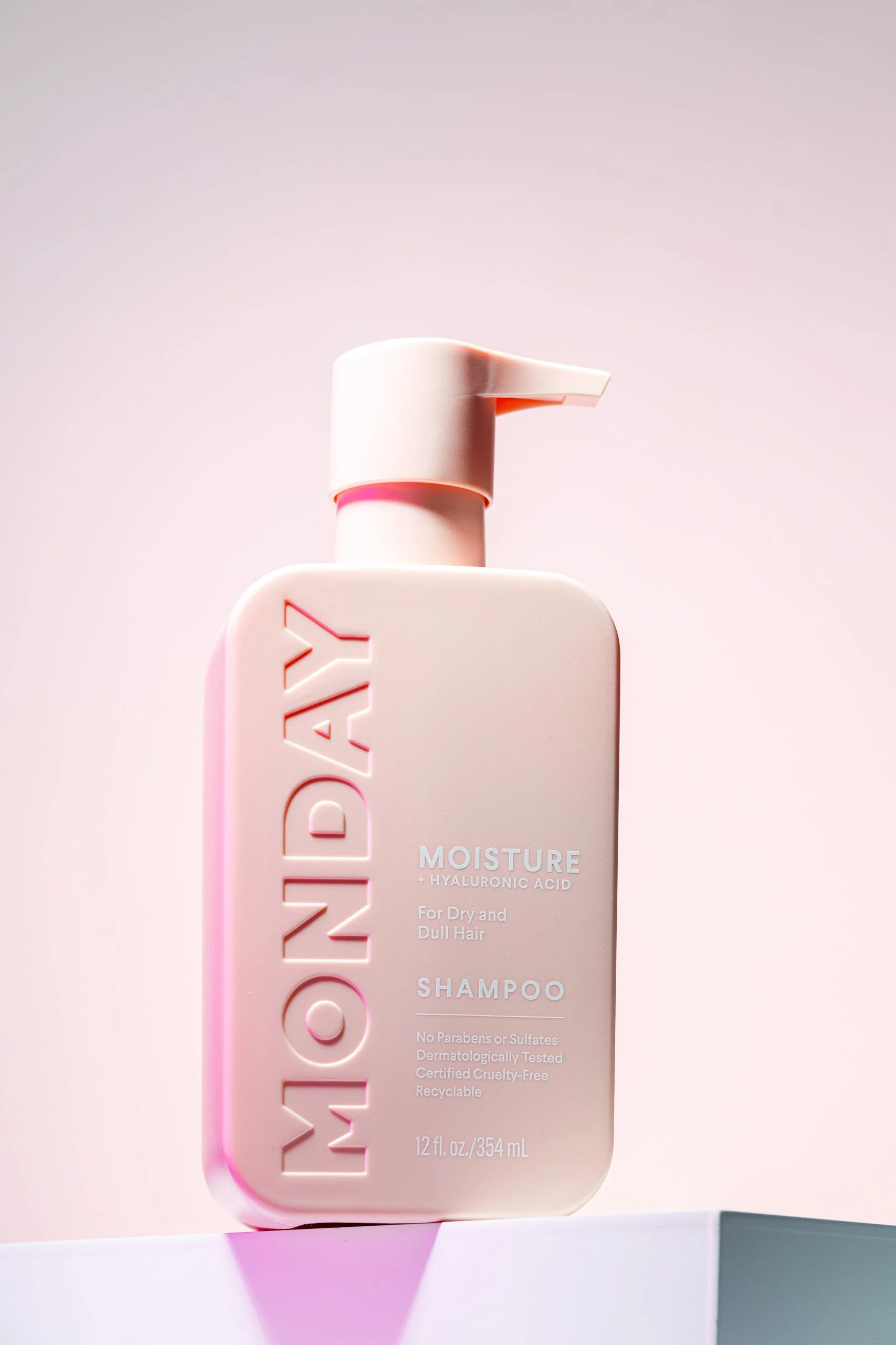 A pink bottle of MONDAY Moisture shampoo for dry and dull hair with hyaluronic acid, featuring a pump dispenser and minimalist label design.