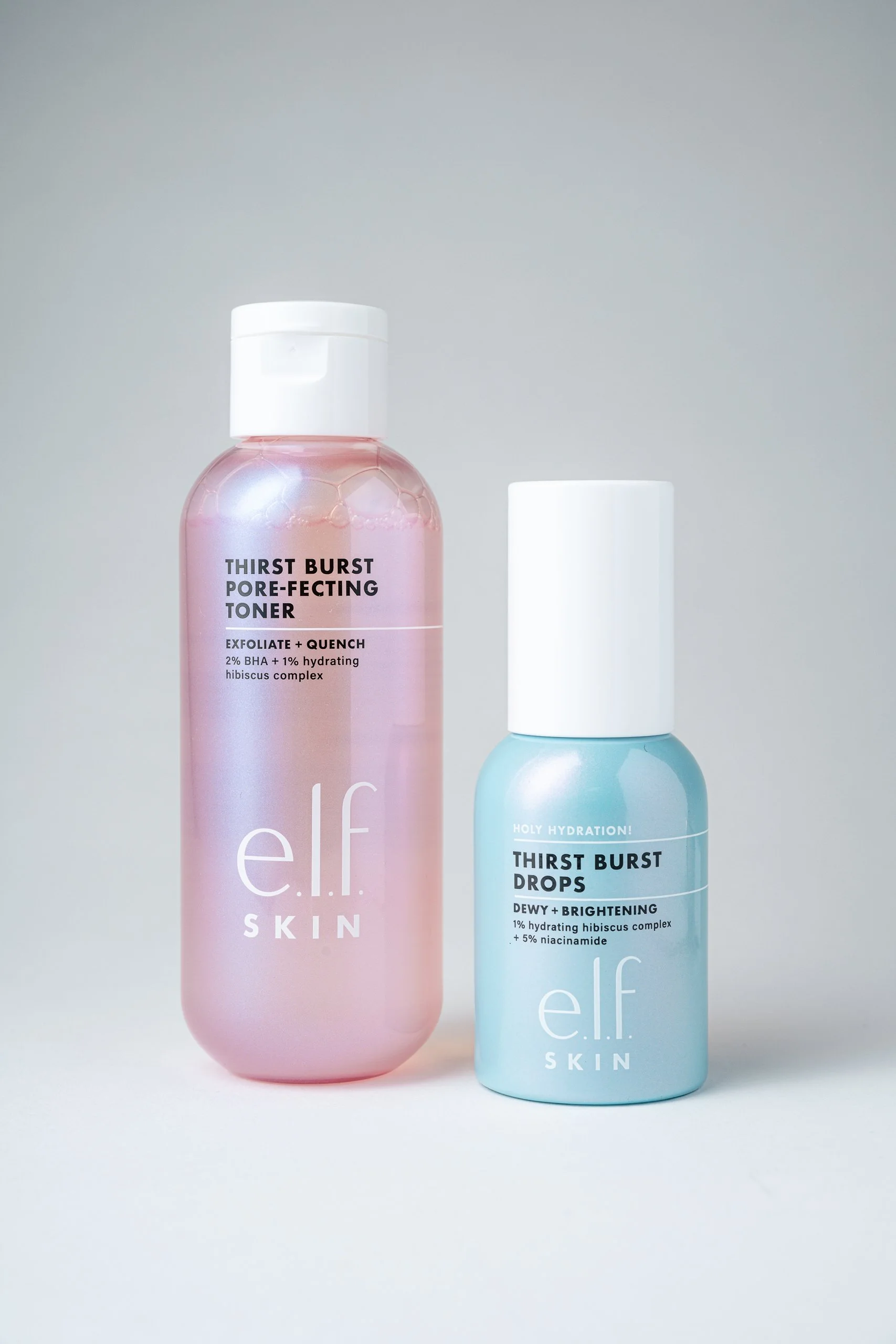 Two bottles of skincare products from elf SKIN, one pink labeled 'Thirst Burst Pore-Perfecting Toner' and one blue labeled 'Thirst Burst Drops,' against a plain light background.