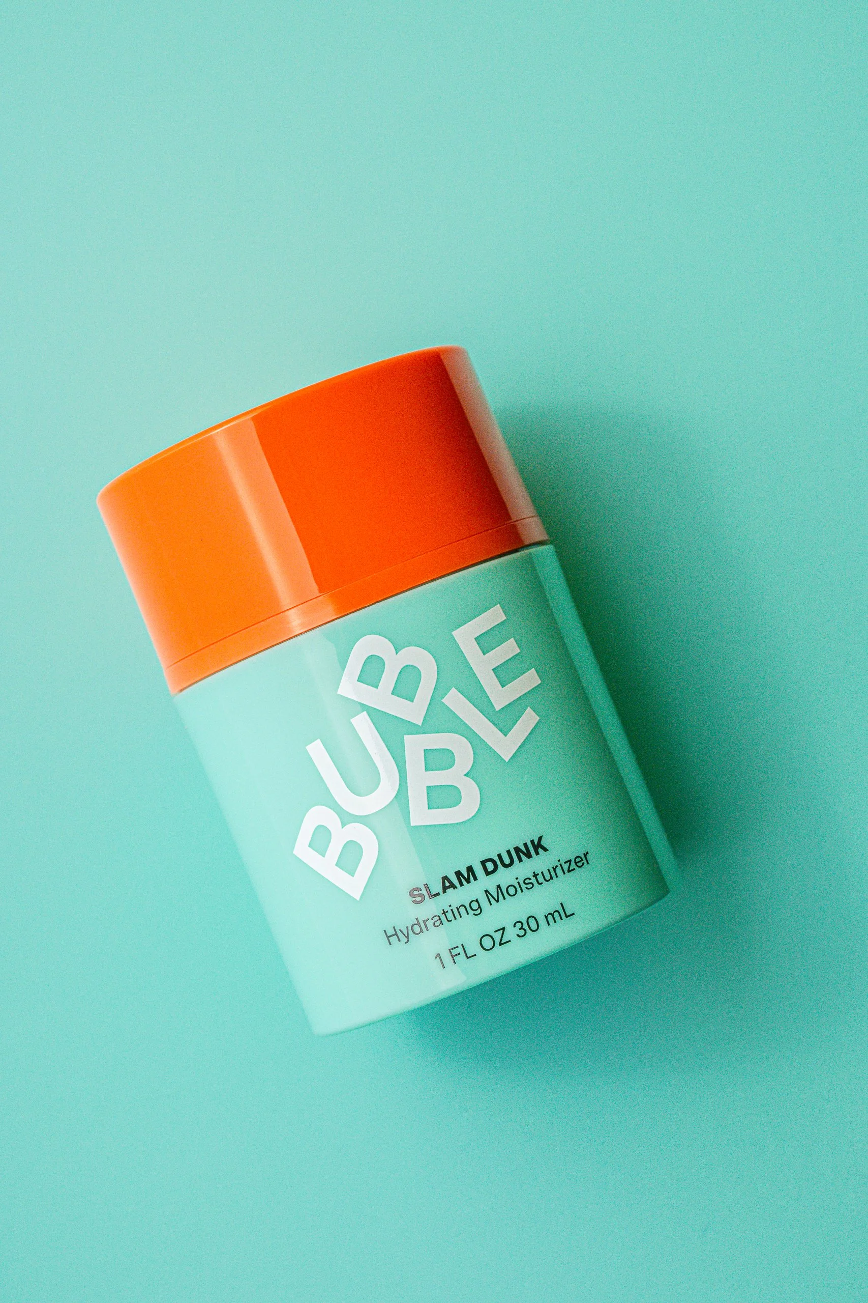 A close-up of a turquoise bottle of hydrating moisturizer with an orange cap on a matching turquoise background.