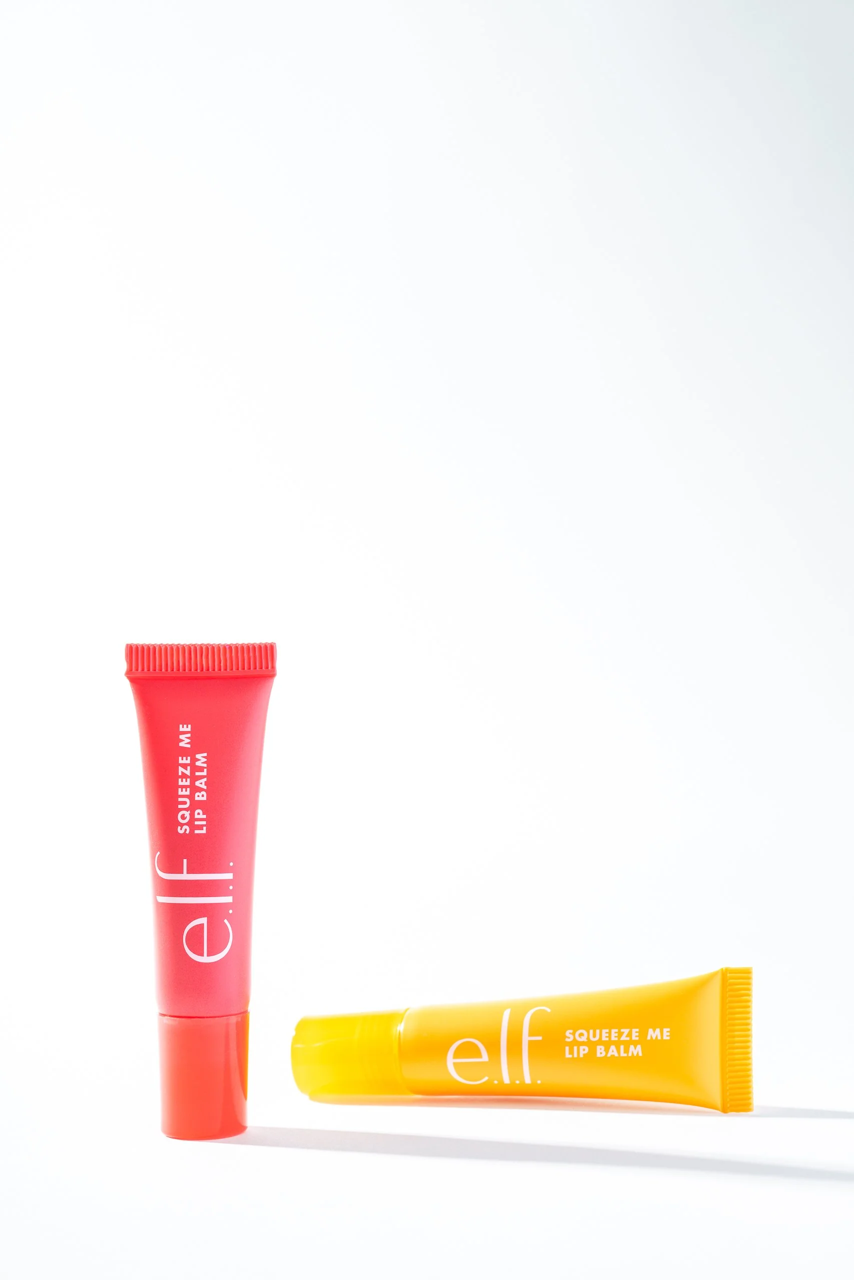 Two tubes of elf Squeeze Me Lip Balm, one pink and one yellow, placed on a white background.
