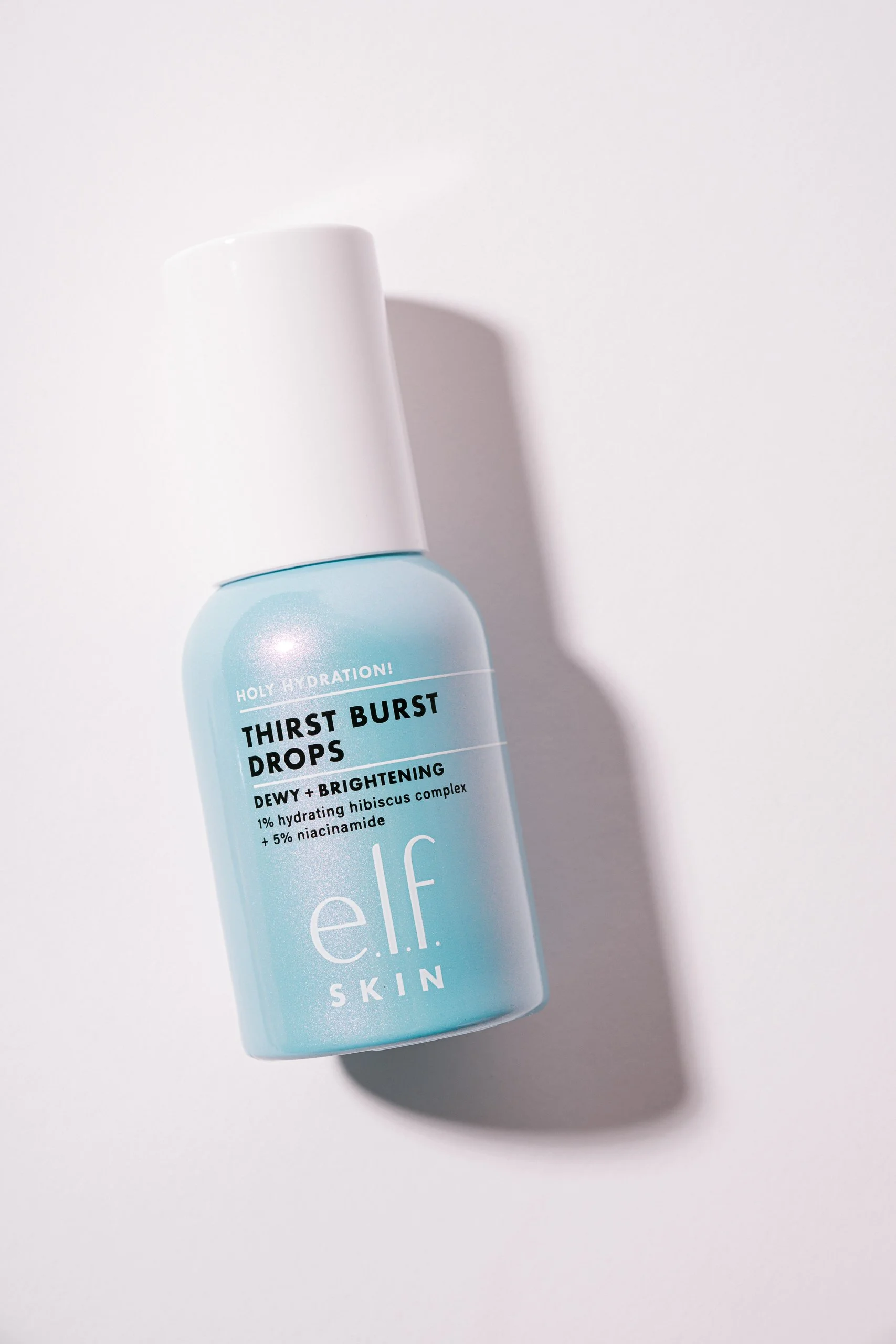 A light blue bottle of e.l.f. skincare product called Thirst Burst Drops located on a white surface, with a clouded shadow to the right.