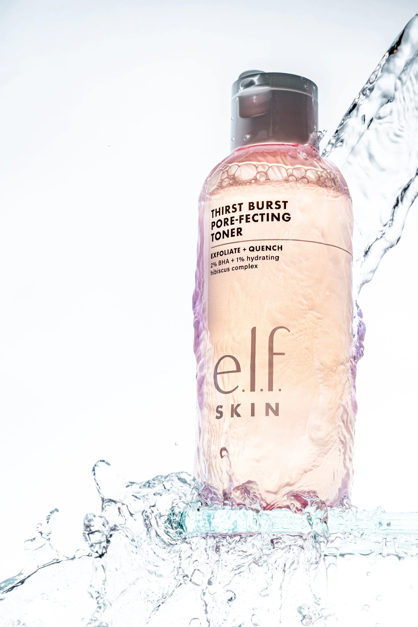 A bottle of e.l.f. SKIN Thirst Burst Pore-Refining Toner surrounded by splashing water, highlighting its hydrating and pore-clearing properties.