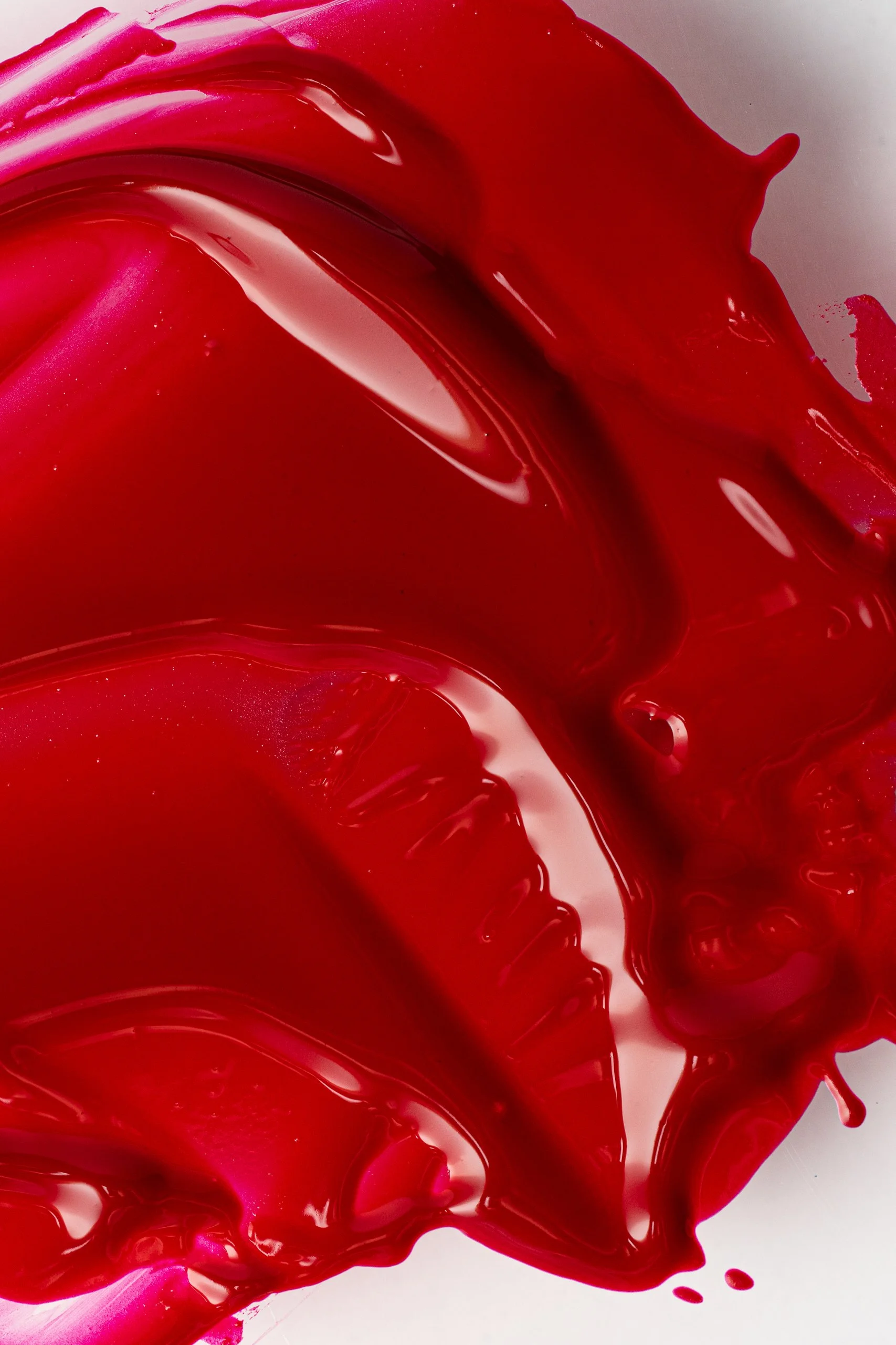 Close-up of red lipstick being spread on a surface, showing glossy texture and flowing patterns.