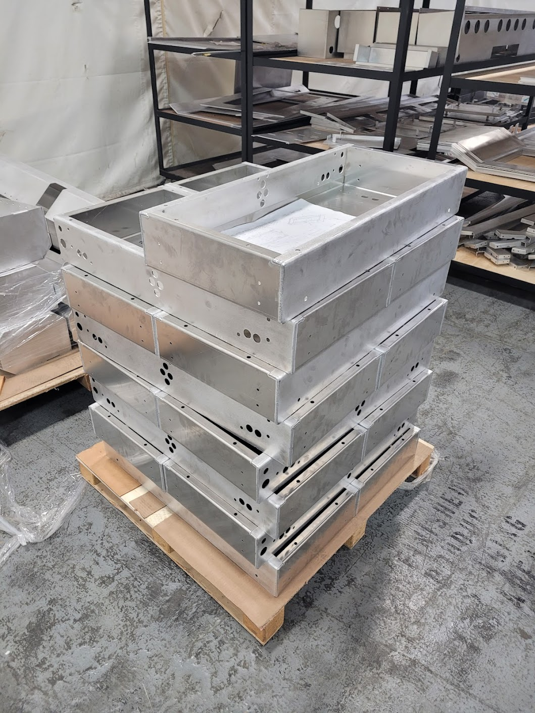 Stack of unfinished metal parts, likely for machinery or equipment, placed on a wooden pallet in an industrial workshop.