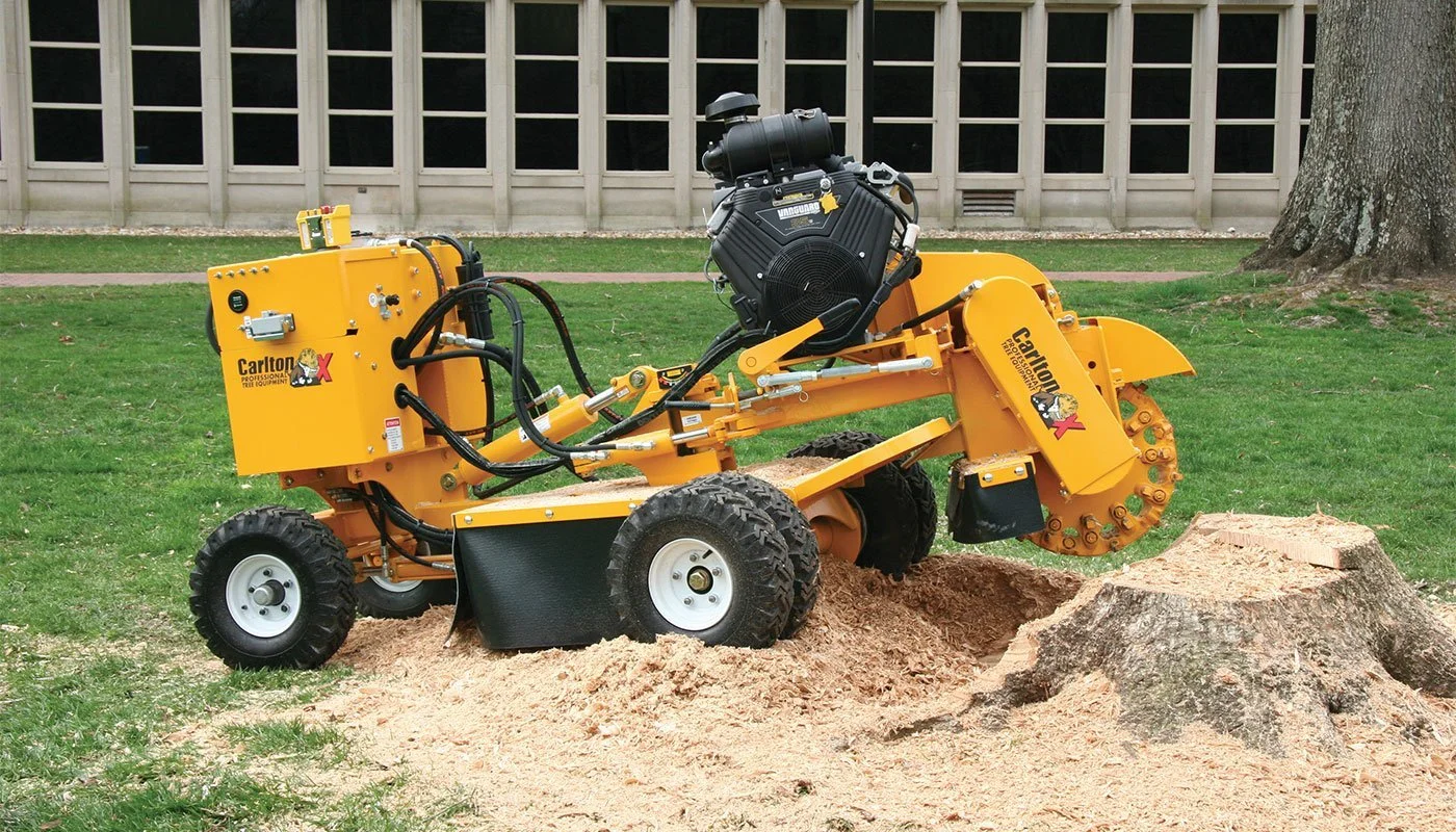 A black and yellow stump grinding machine operating on a tree stump in a grassy area outside.