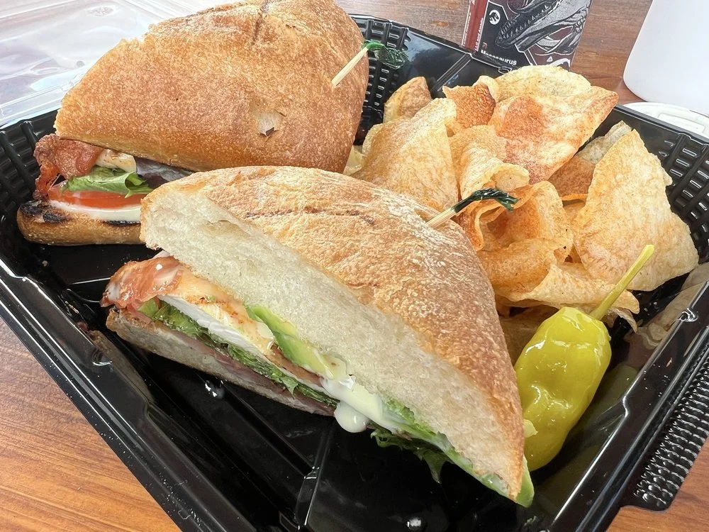 A black tray containing two sandwiches, a pile of potato chips, and two pickled peppers.