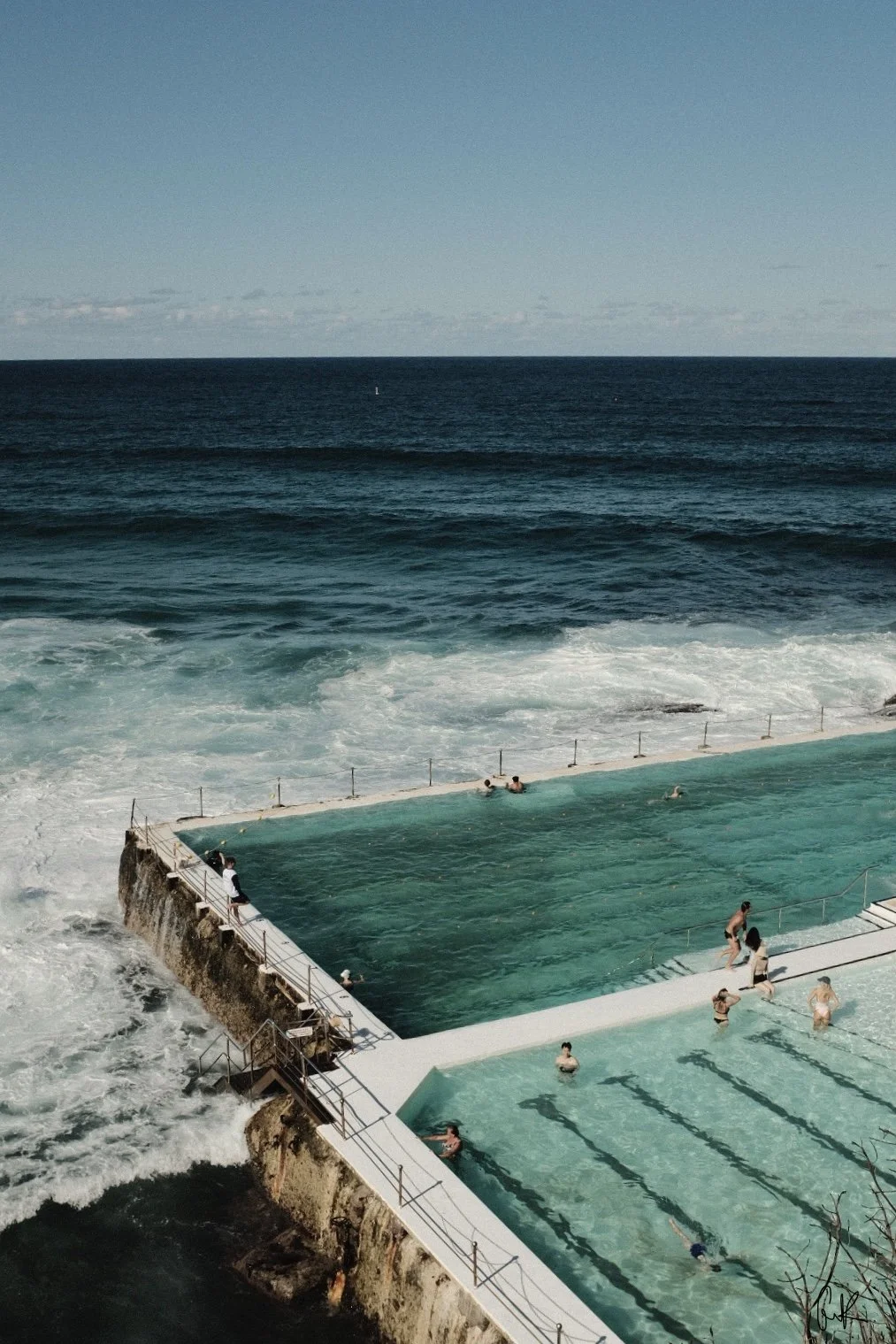 People swimming and relaxing in an ocean pool near the shoreline with waves crashing against the edge.