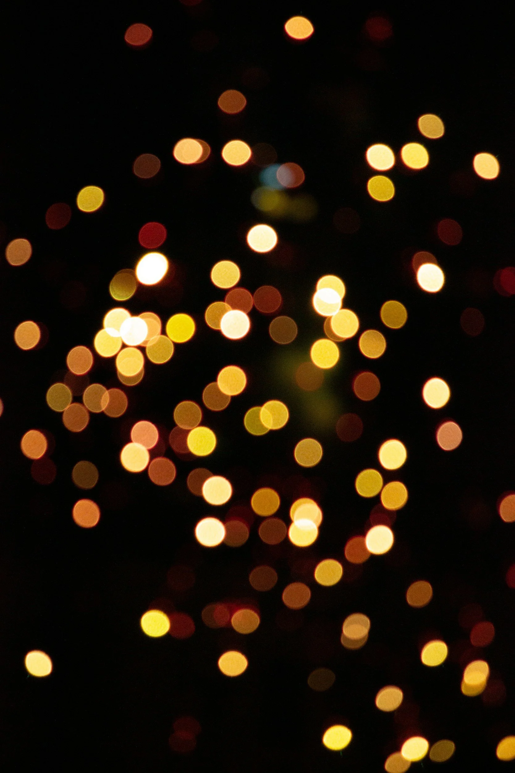 Blurred string lights with warm yellow, orange, red, and some blue lights against a dark background.