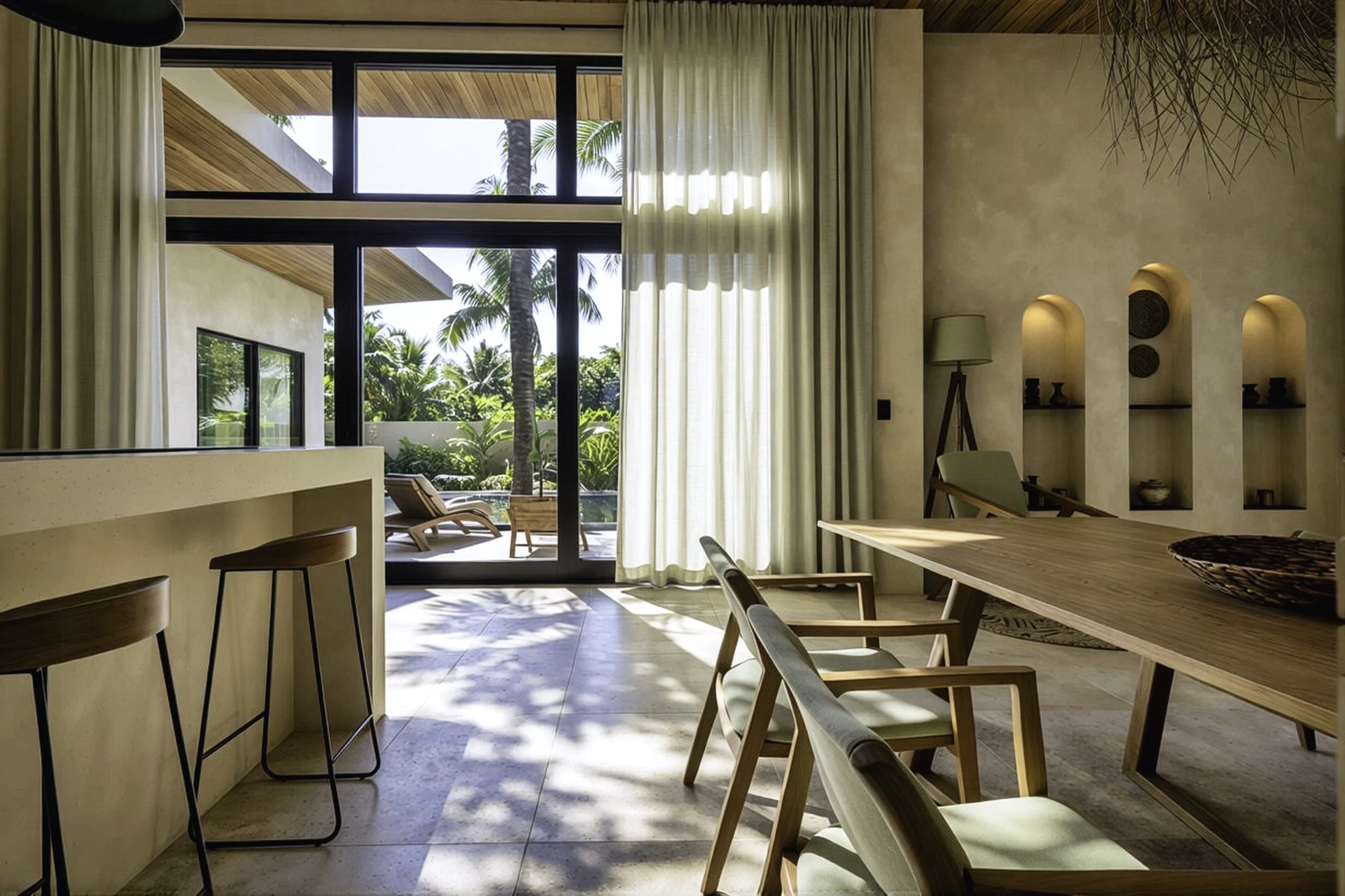 Bright, modern interior living space with large glass sliding doors opening to a tropical outdoor patio with lounge chairs, lush green palm trees, and clear blue skies.