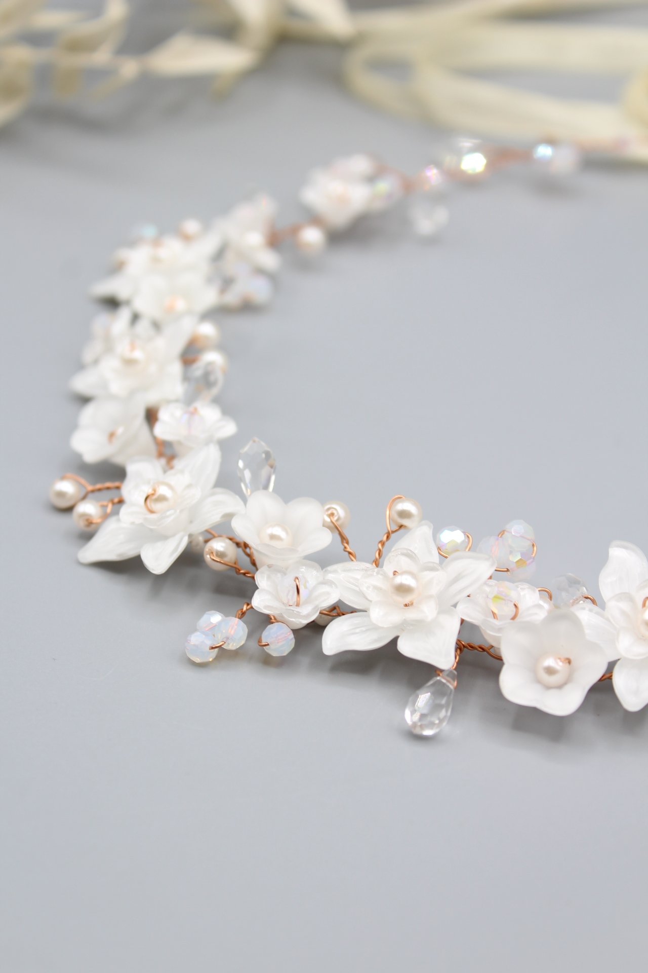 Ein Chinese-Haarband mit weißen Blumen und glitzernden Kristall- und Perlenakzenten auf einem grauen Hintergrund.