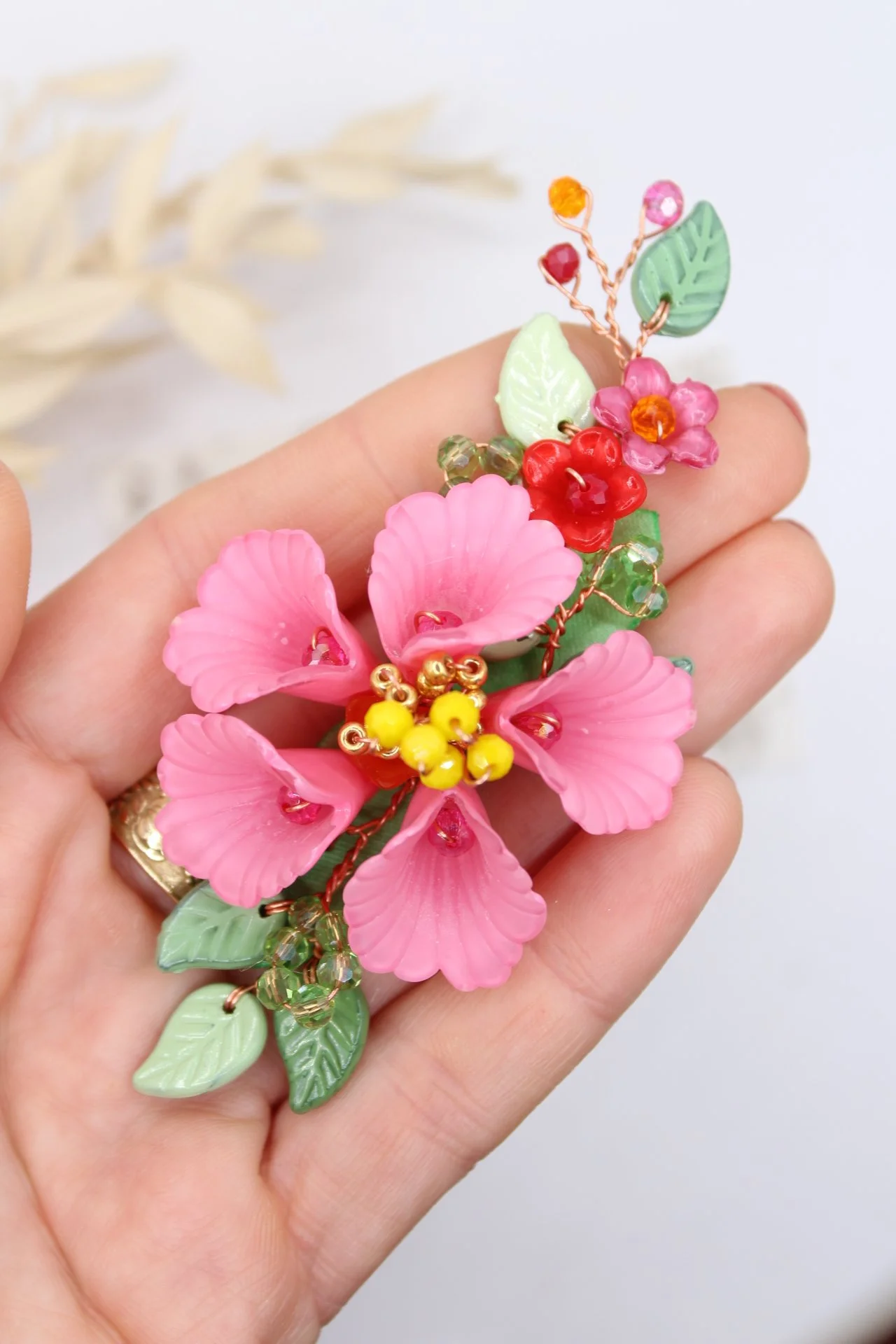 Grosser pinker Blütenbrosche mit grünen Blättern und bunten kleinen Beeren auf einer Hand