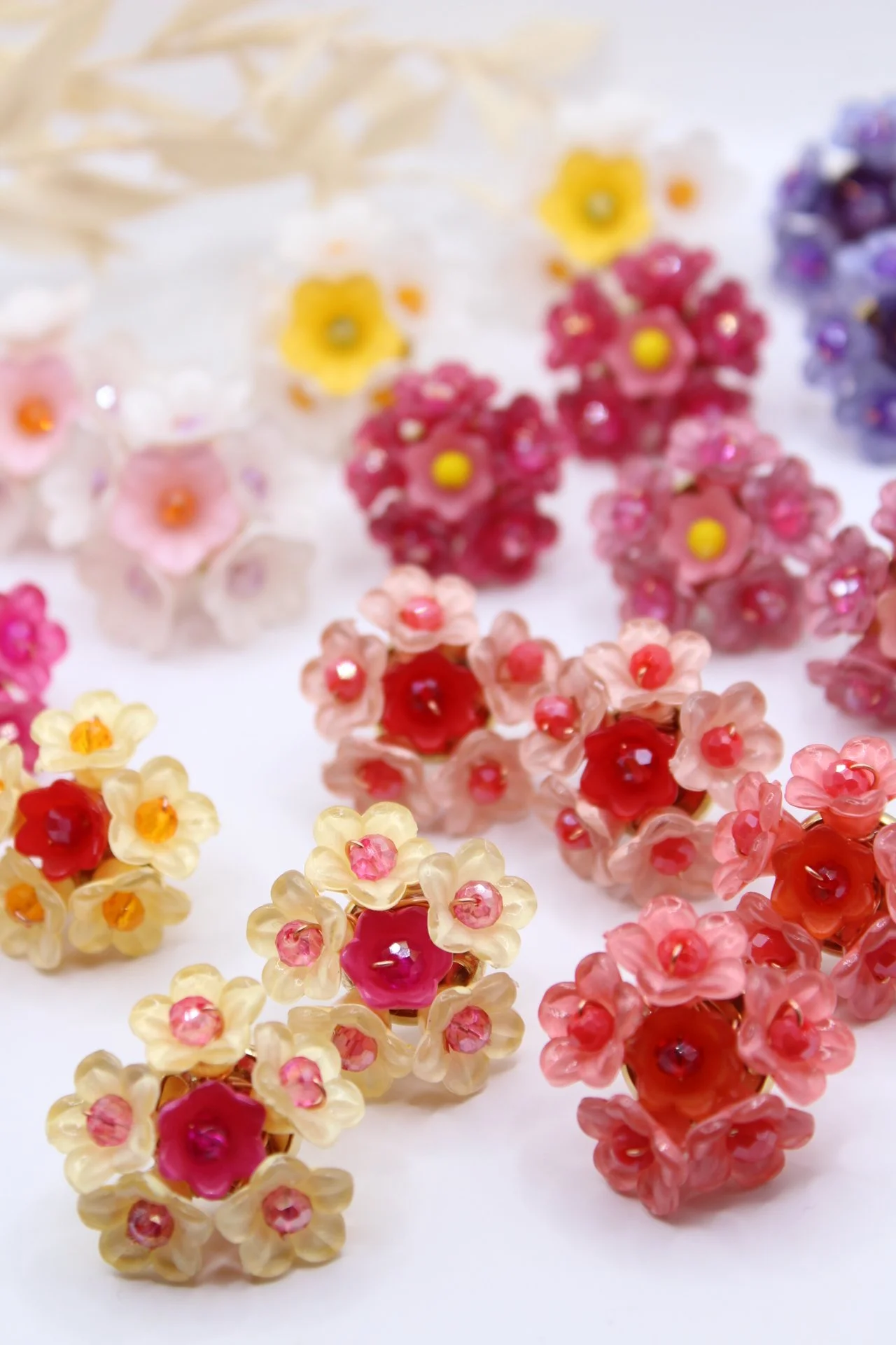 Bunte Perlen in Form von Blumen in verschiedenen Farben, darunter Gelb, Rosa, Rot und Violett, auf weißem Hintergrund.