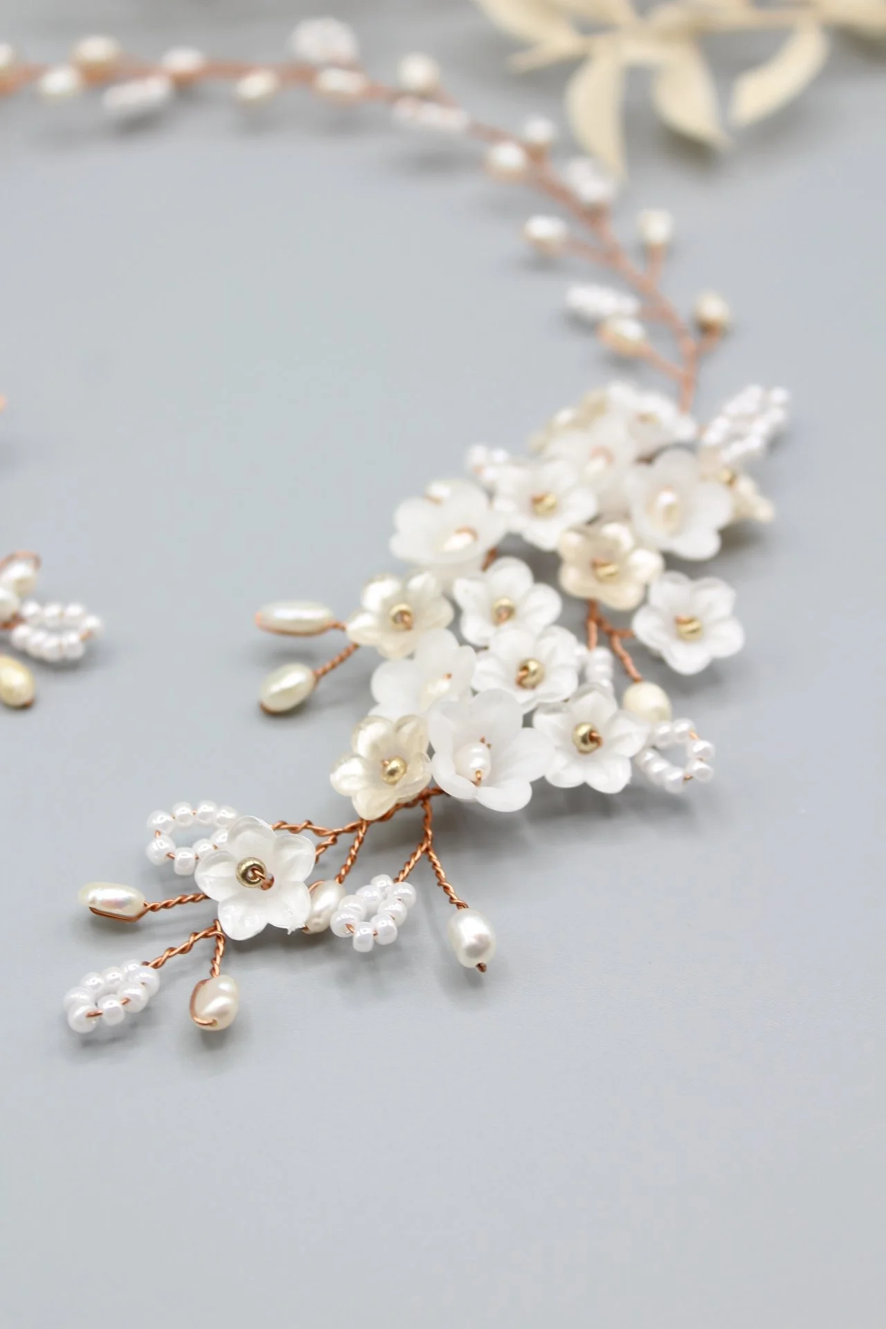 Eine Perlen- und Blumen-Haarreif mit weißen Blüten und goldenen Details auf grauem Hintergrund.