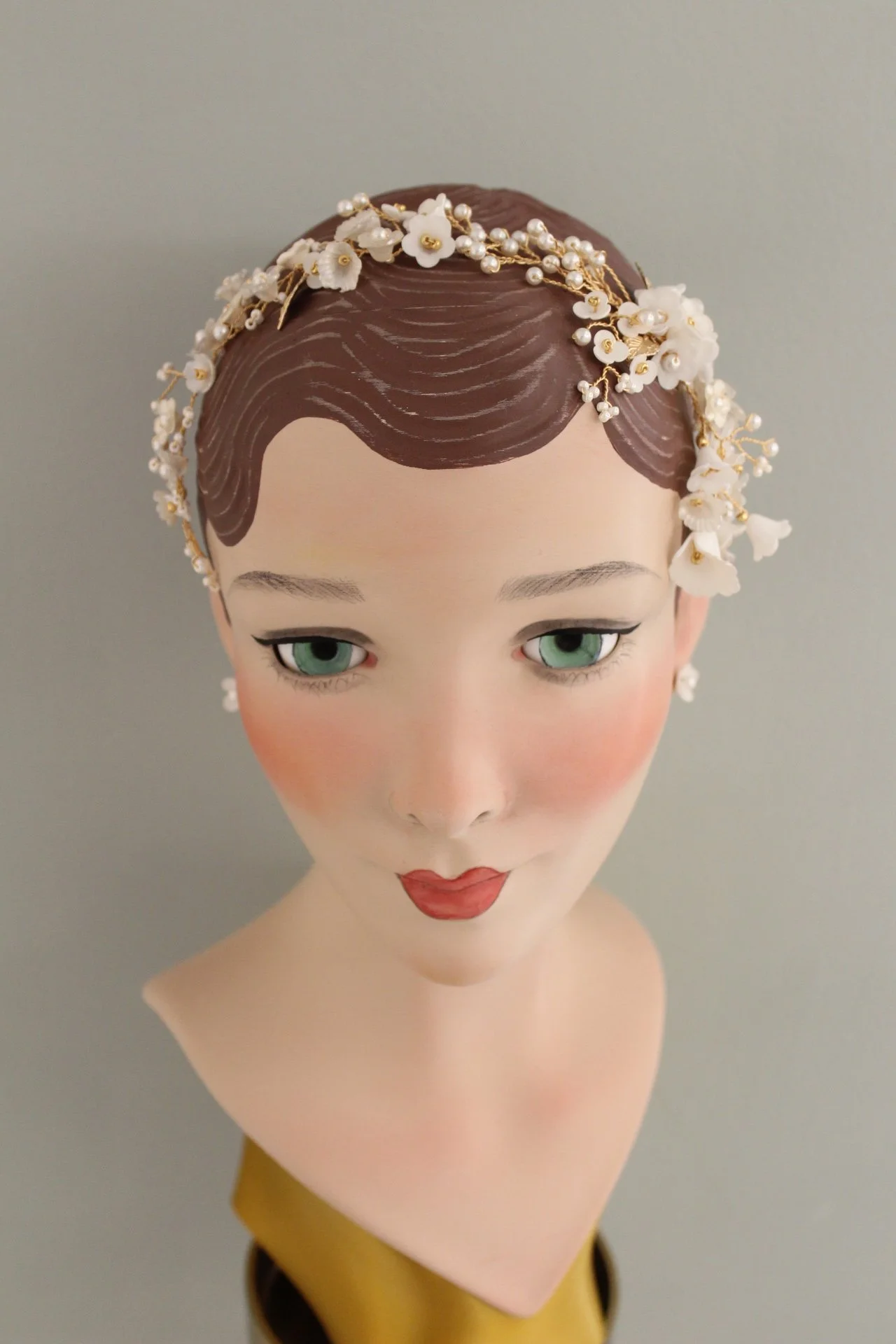 Dekofigur einer stilisierten Frau mit braunem Haar und Spitze, mit weißen Blumen und Perlen im Haar, trägt roten Lippenstift, hat grüne Augen und trägt Ohrringe.