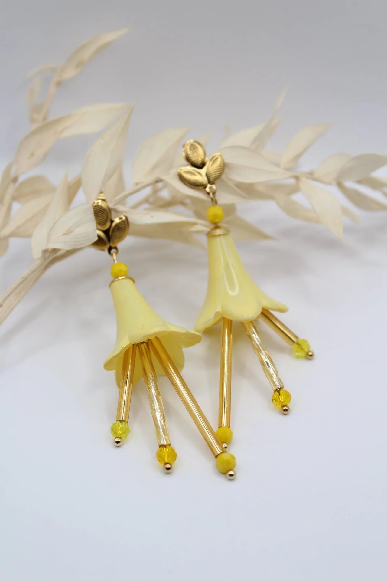 Goldene und gelbe Blumenohrringe mit Blütendesign und Perlen, vor einem weißen Hintergrund