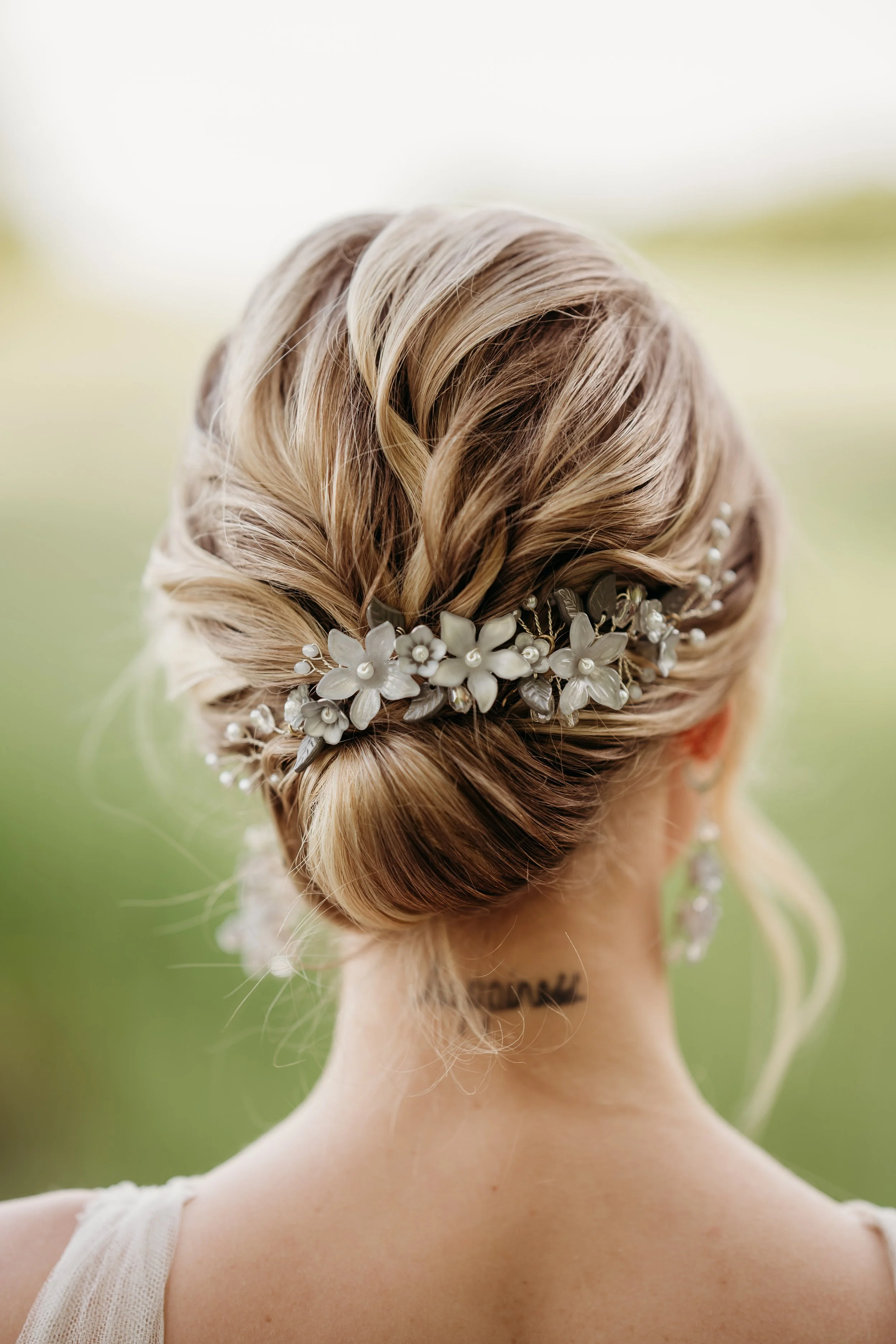 Hochzeitsfrisur mit einer dekorativen Haarblume und Perlen, die am Hinterkopf einer Frau angeordnet ist.