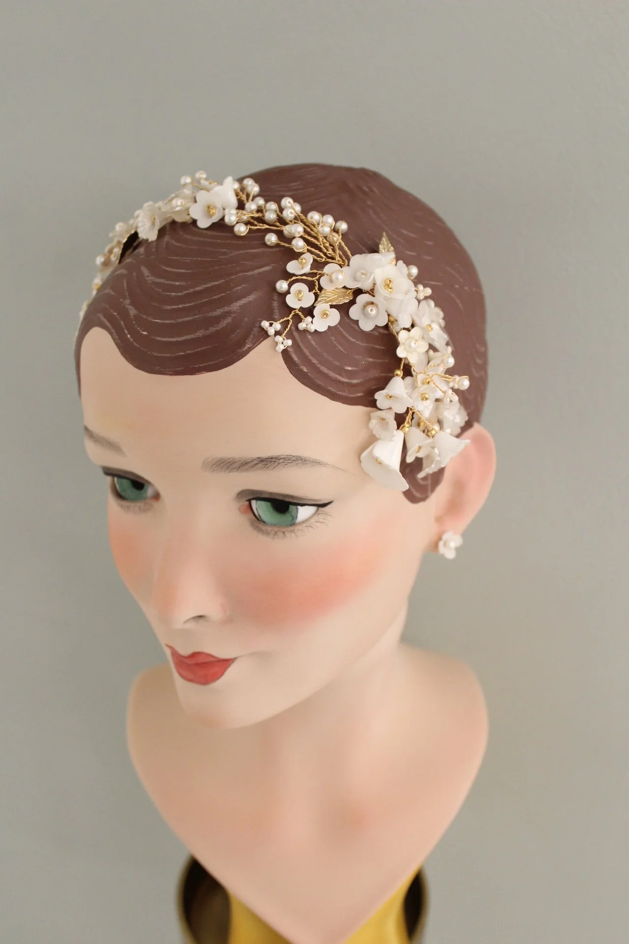 Puppenmodell mit braunem Haarschmuck, weißen Blumen und Perlen, leicht makeup und rotem Lippenstift.