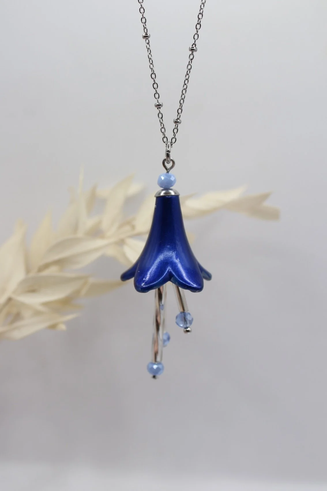 Halskette mit blauer Blumen-Design Anhänger und blauen Kristallen gegen einen neutralen Hintergrund.
