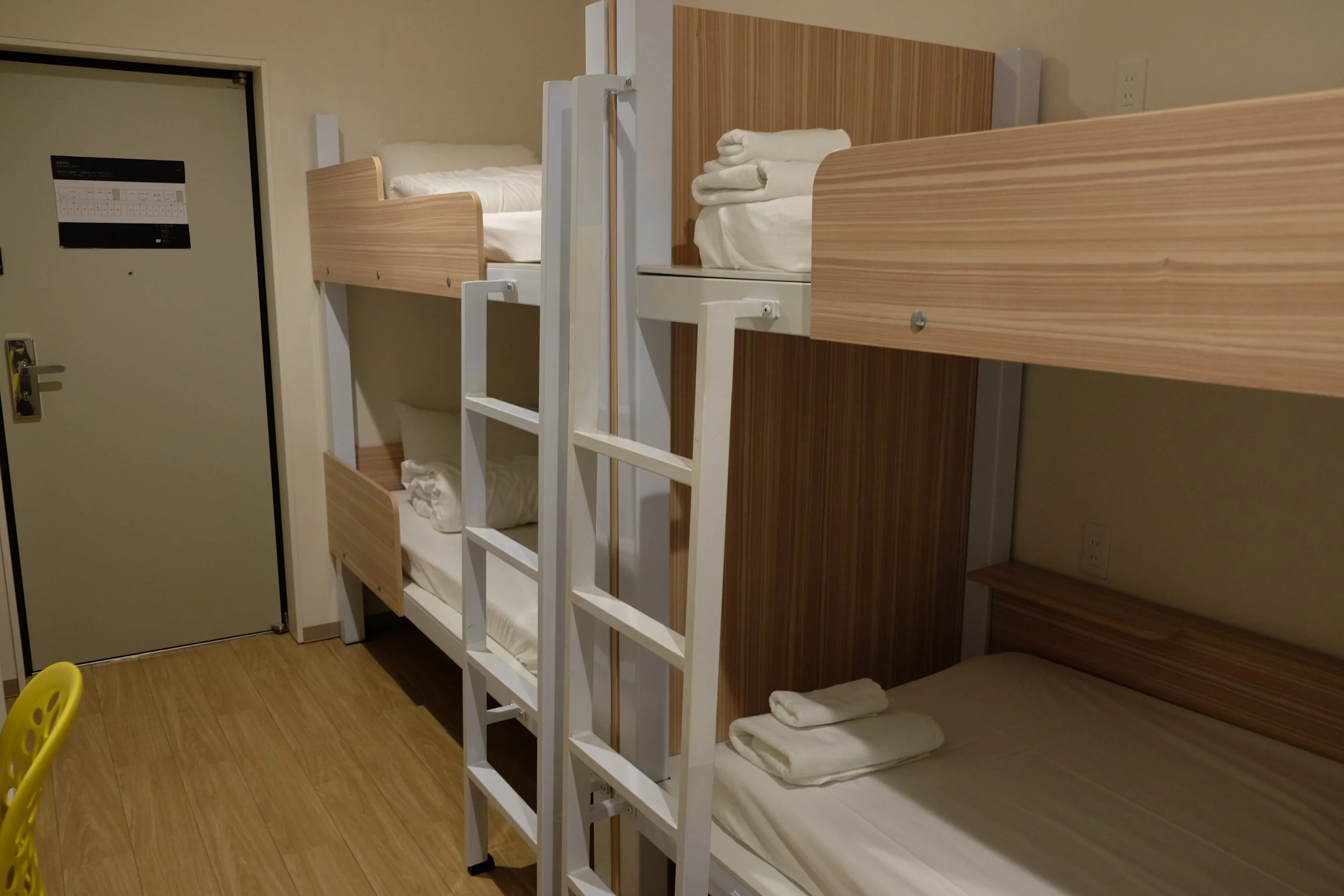 A set of Canadian bunk beds with white frames and light brown wood paneling, neatly made with white linens and rolled towels on top of each bed in a hotel room.