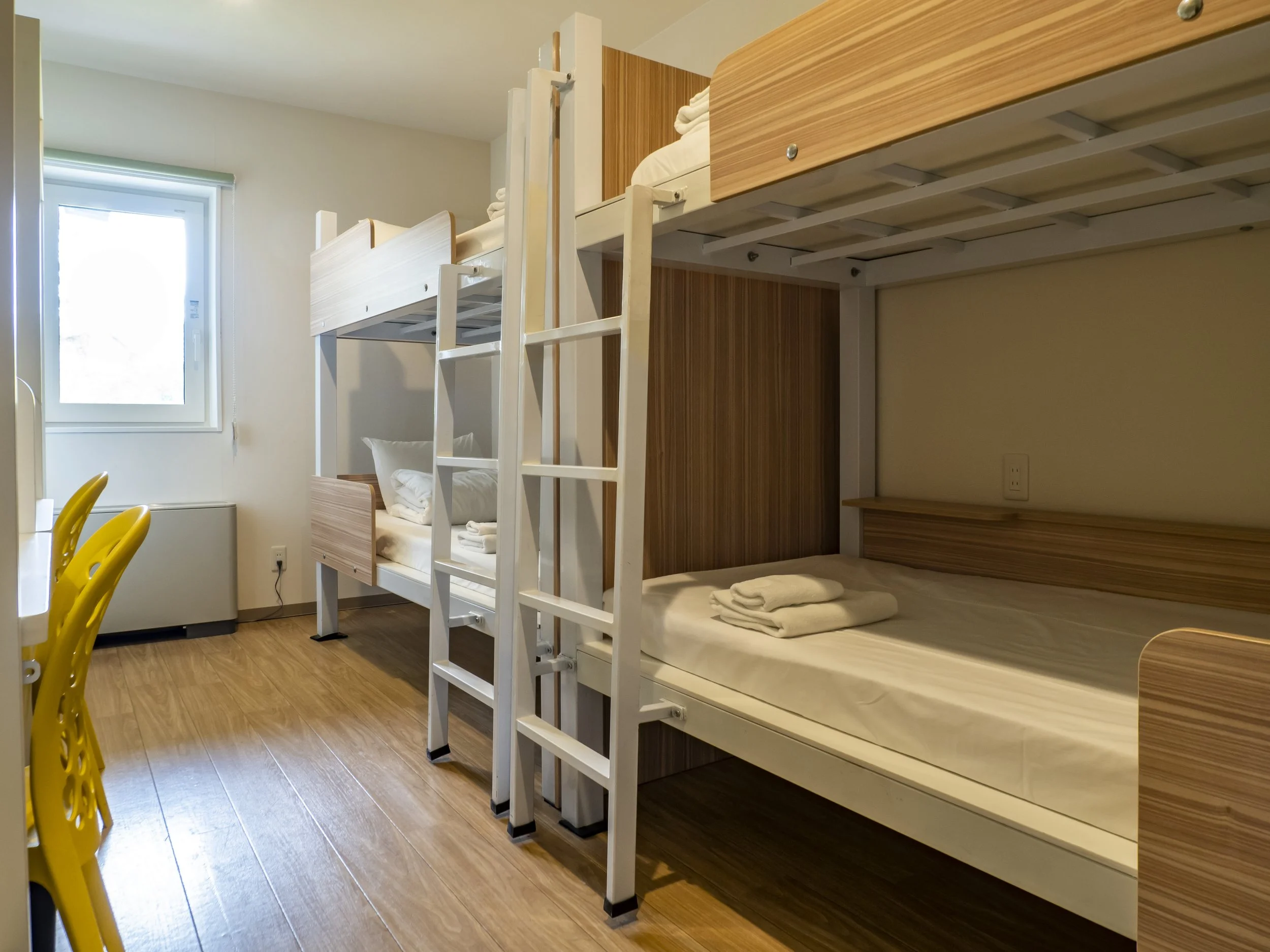 A dormitory room with a bunk bed, a window, and a yellow chair.