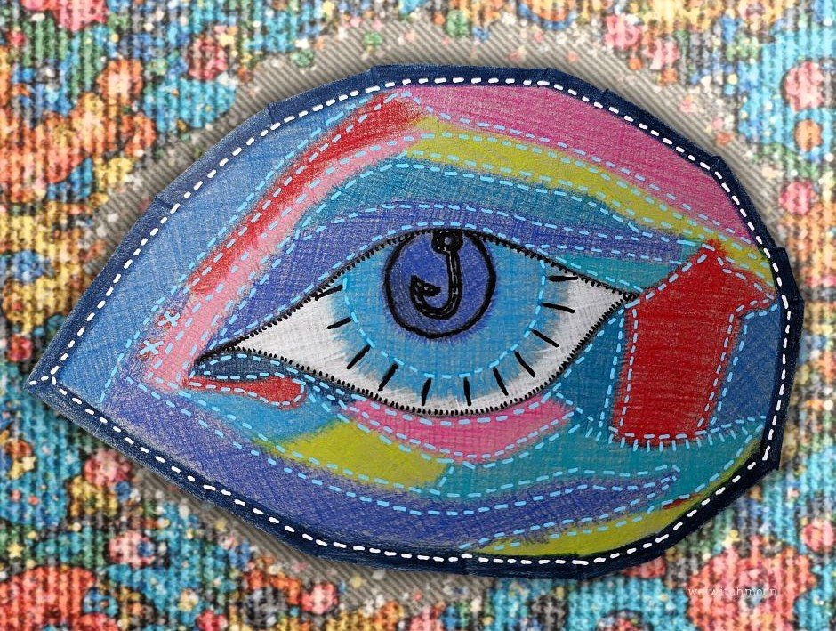 Colorful embroidered patch of an eye with a rainbow-colored iris, set on a textured background.