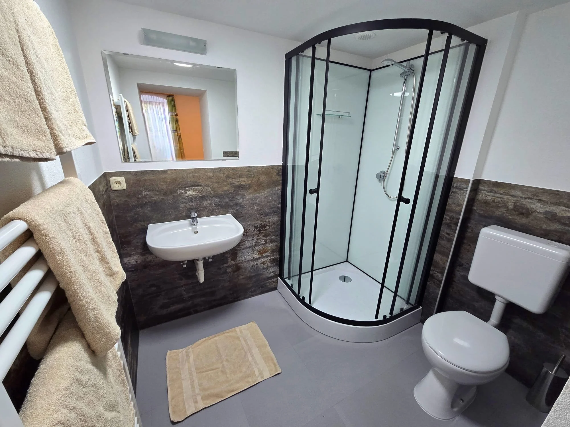 Ein Badezimmer mit Dusche, Waschbecken, Toilette und Handtüchern an der Heizung.