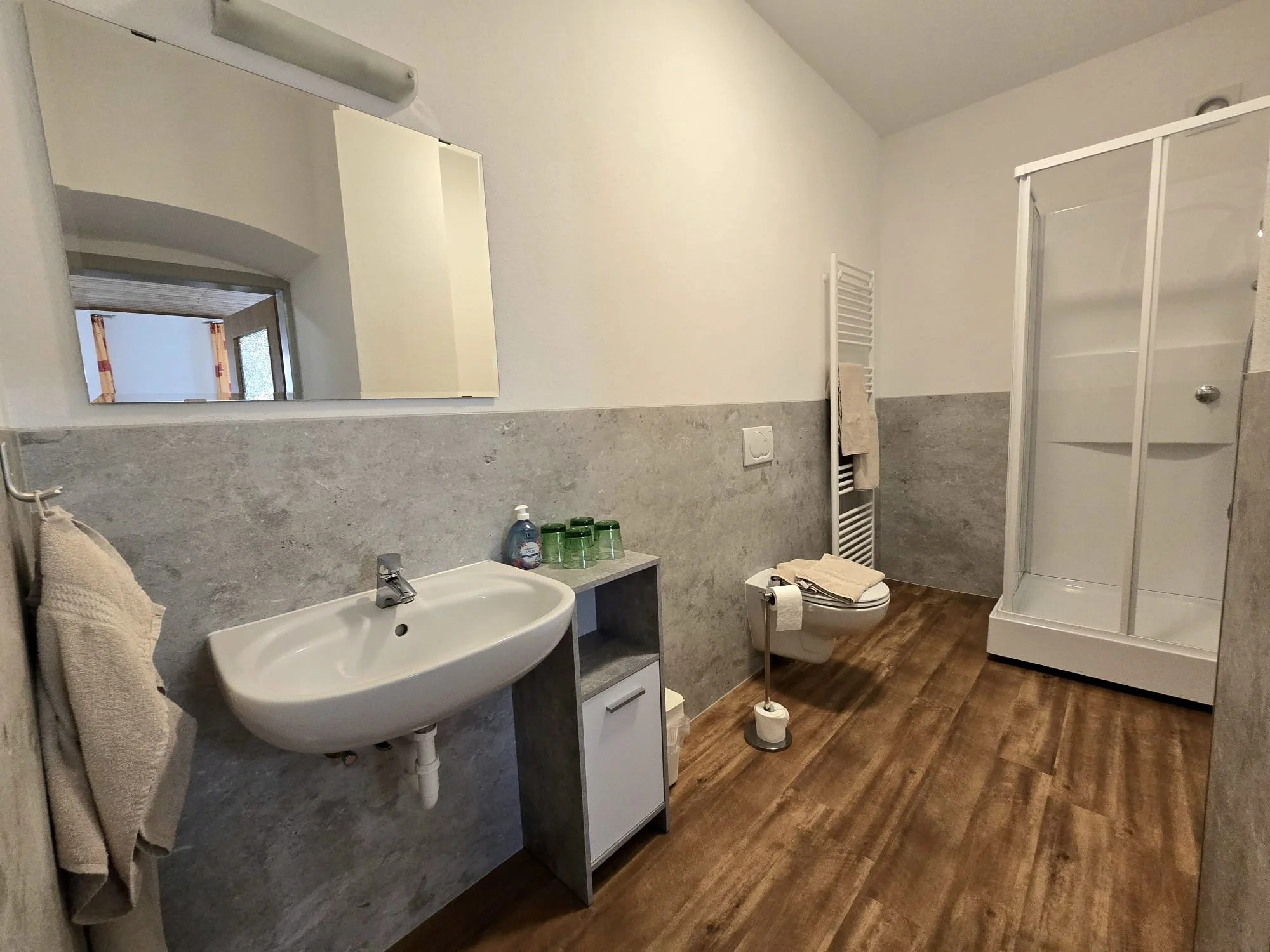 Ein Badezimmer mit Waschbecken, Spiegelschrank, Handtuch, Toilette, Badewanne und Holzfußboden.