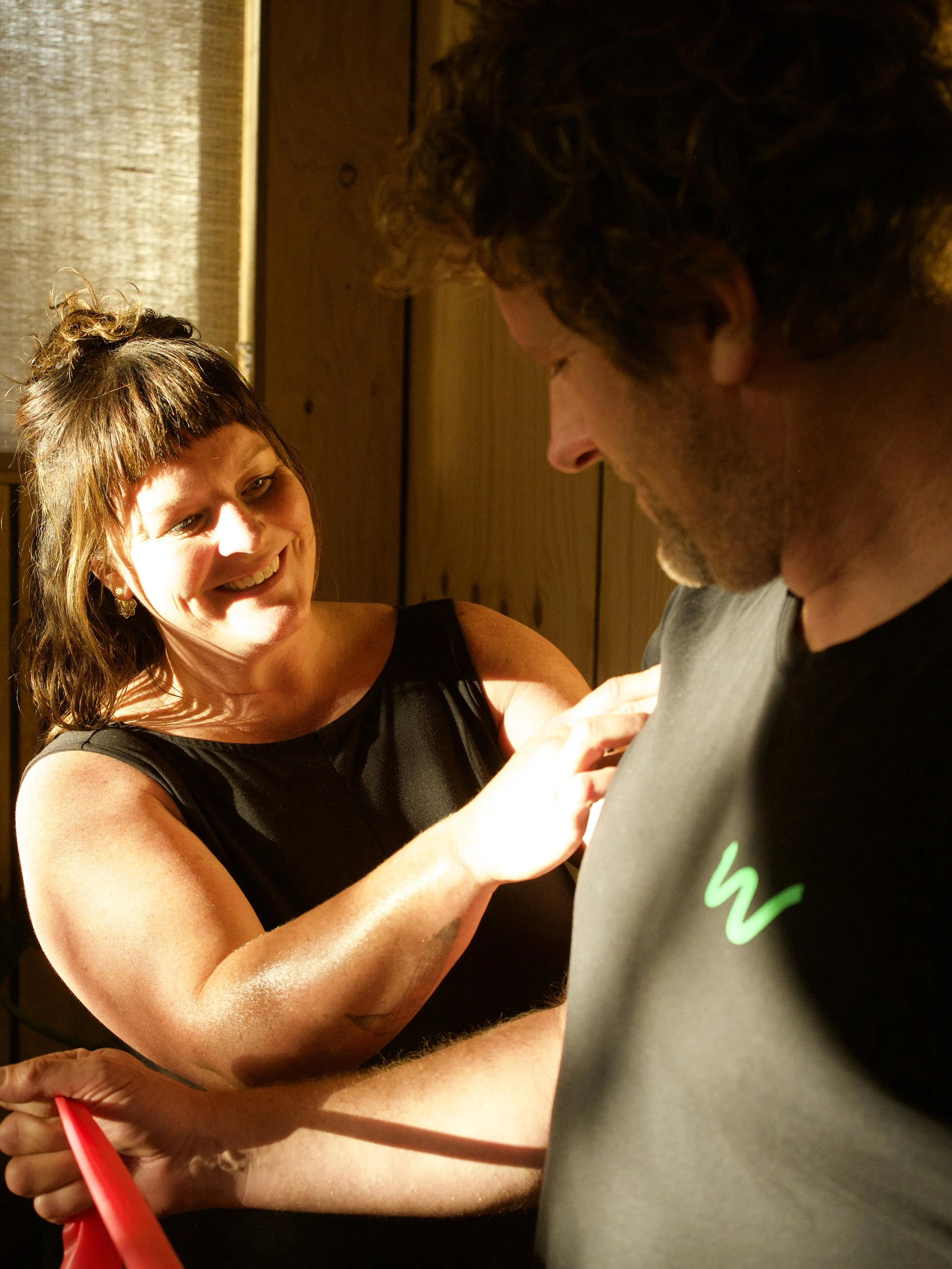 A woman smiling while assessing a clients shoulder.