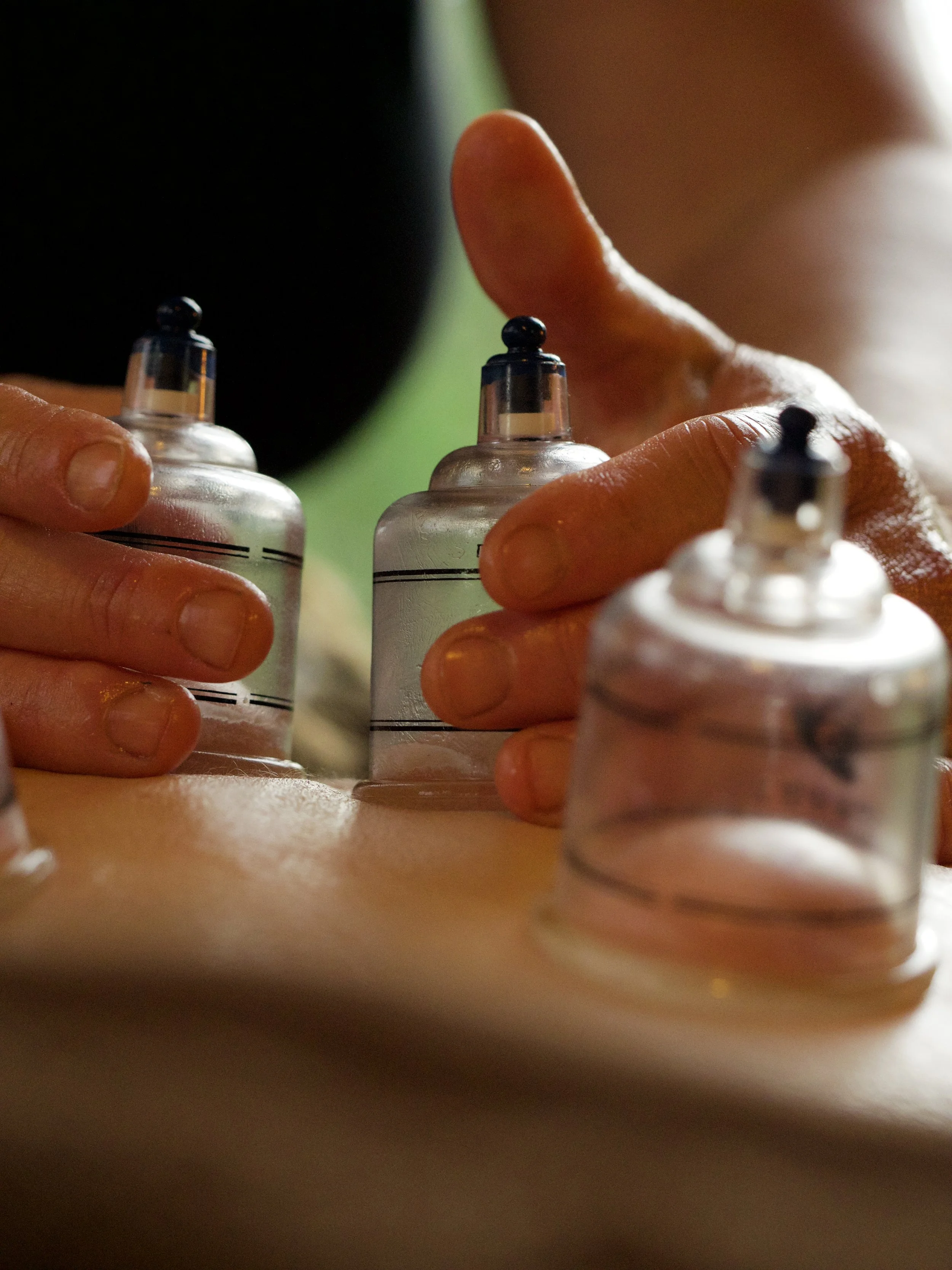 Close-up of hands holding small bottles, possibly ink or paint, with a blurred background.