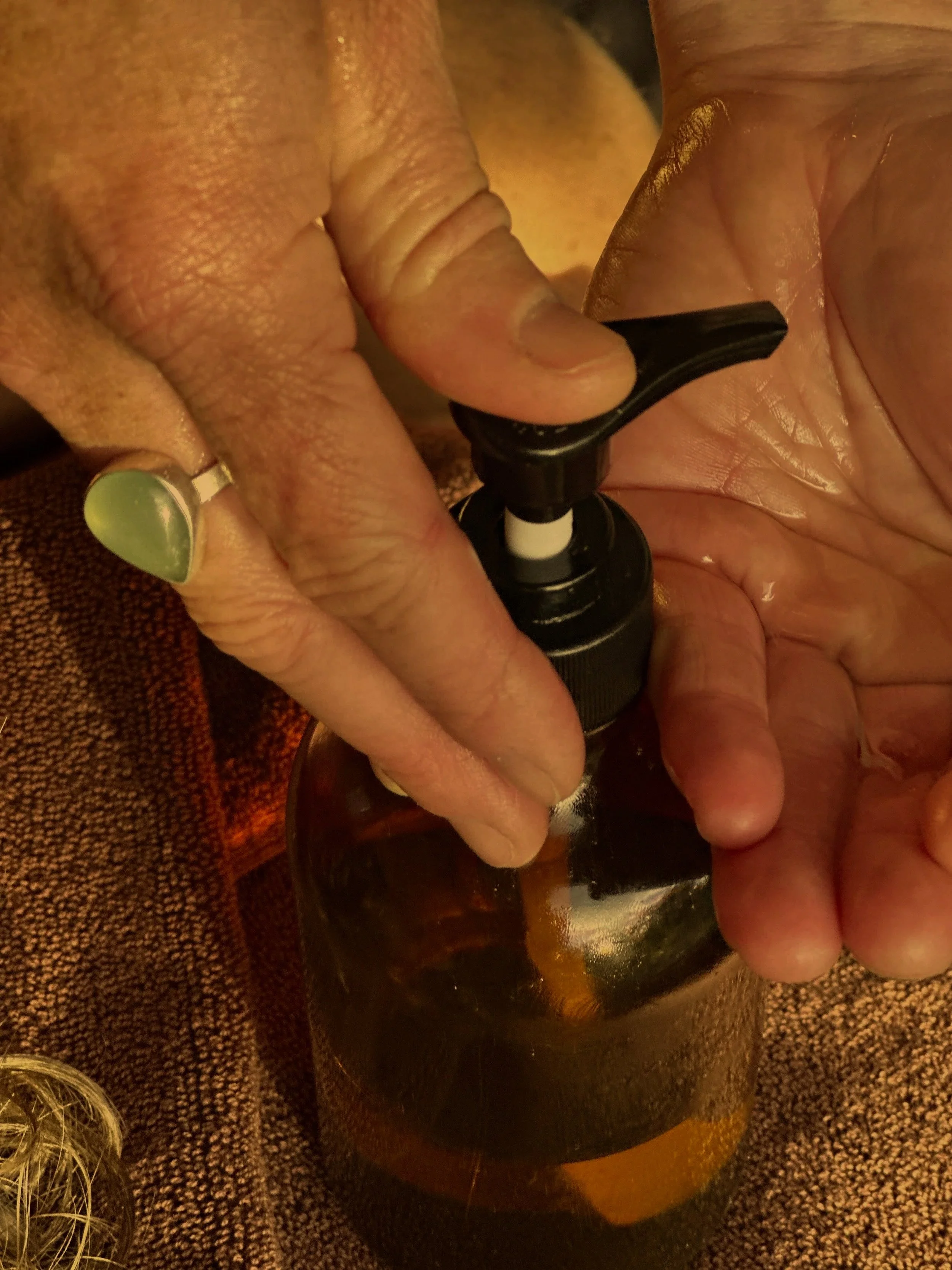 Close-up of a person's hand with painted nails holding a dark glass bottle, possibly a beer bottle.