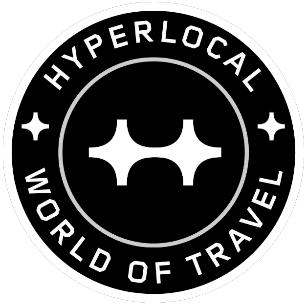 A circular black and white logo for Hyperlocal World of Travel, featuring a central graphic resembling a stylized bridge or arch.