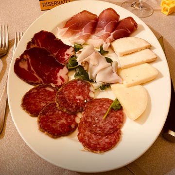 Assorted cured meats and cheeses on a white plate, including prosciutto, mortadella, slices of white cheese, and slices of red salami.