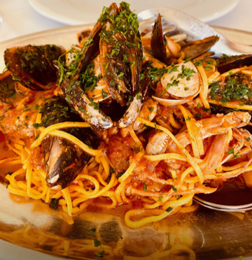 Linguine pasta with a mix of seafood including mussels, clams, and shrimp, garnished with chopped herbs.
