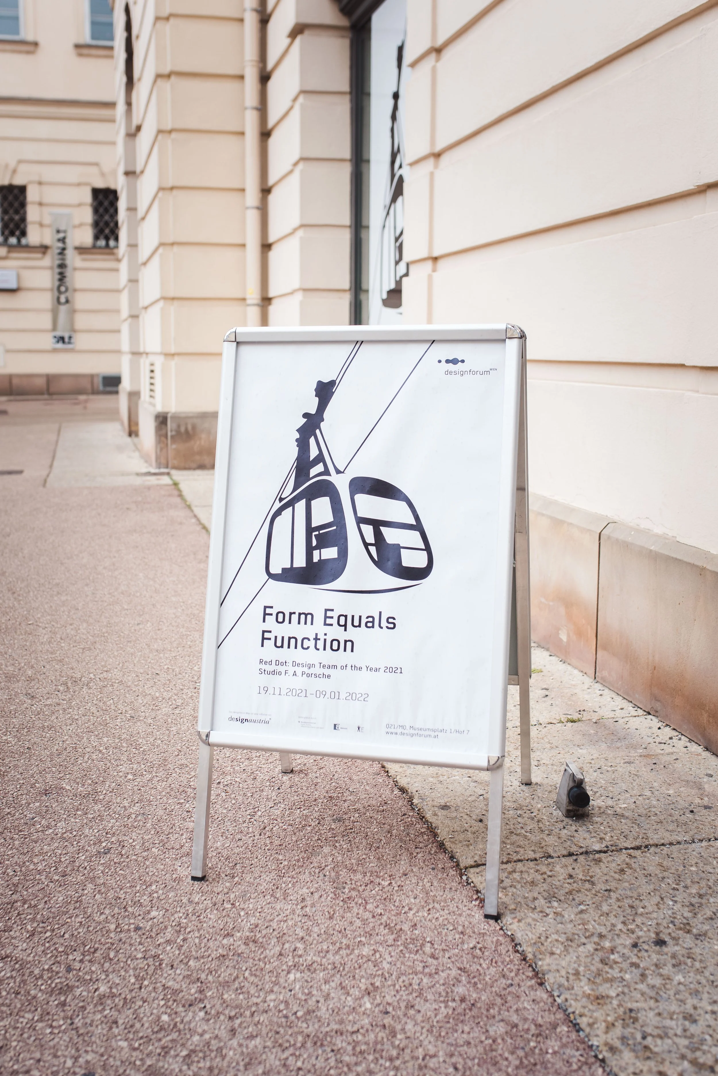 Werbetafel für eine Ausstellung namens "Form Equals Function" vor einem Gebäude, informiert über die Ausstellung vom 19.11.2021 bis 09.01.2022.