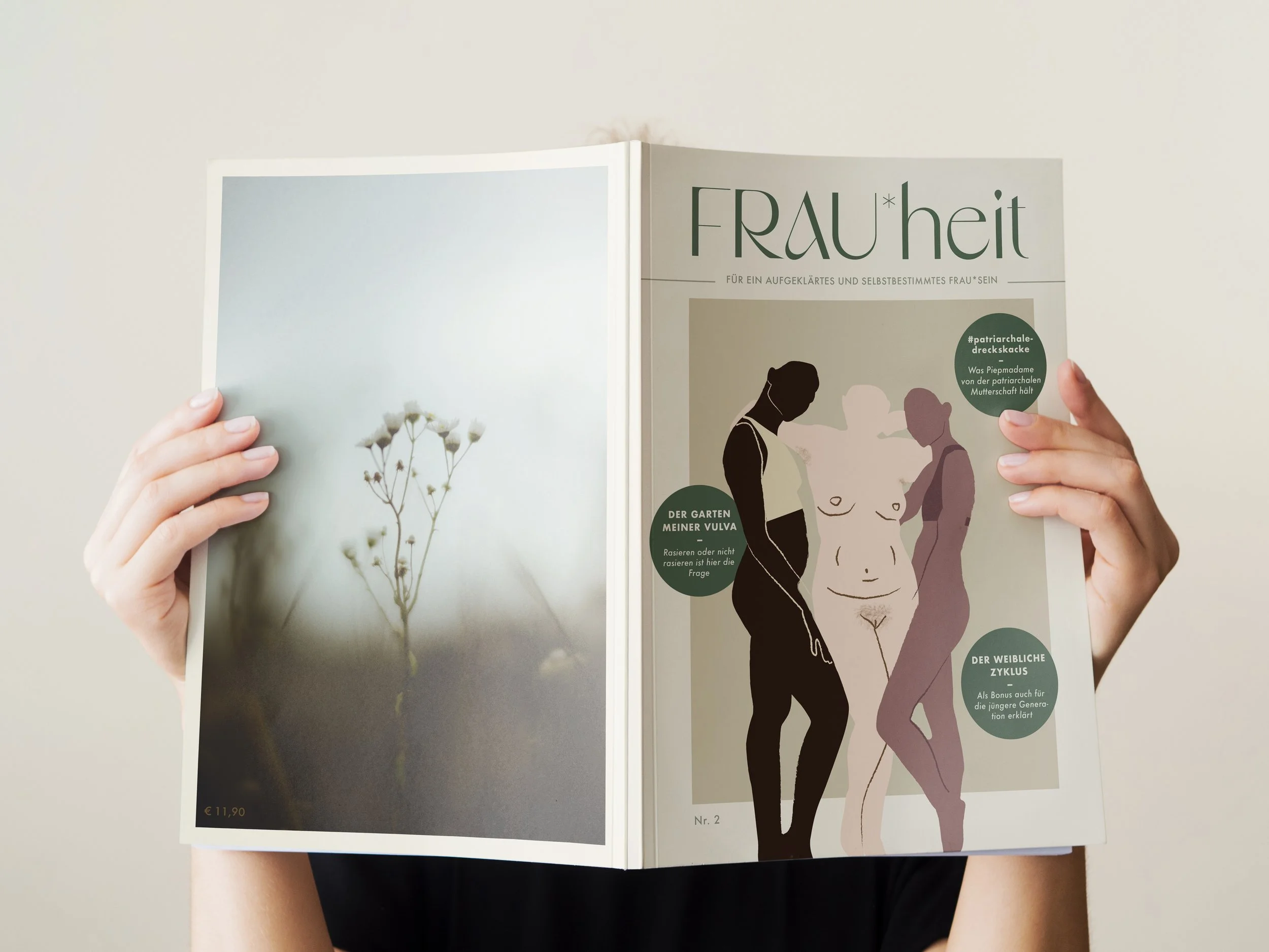 A person holding an open magazine with a subdued nature photo on the left page and an illustrated cover on the right page. The cover features stylized silhouettes of two women and text in German.