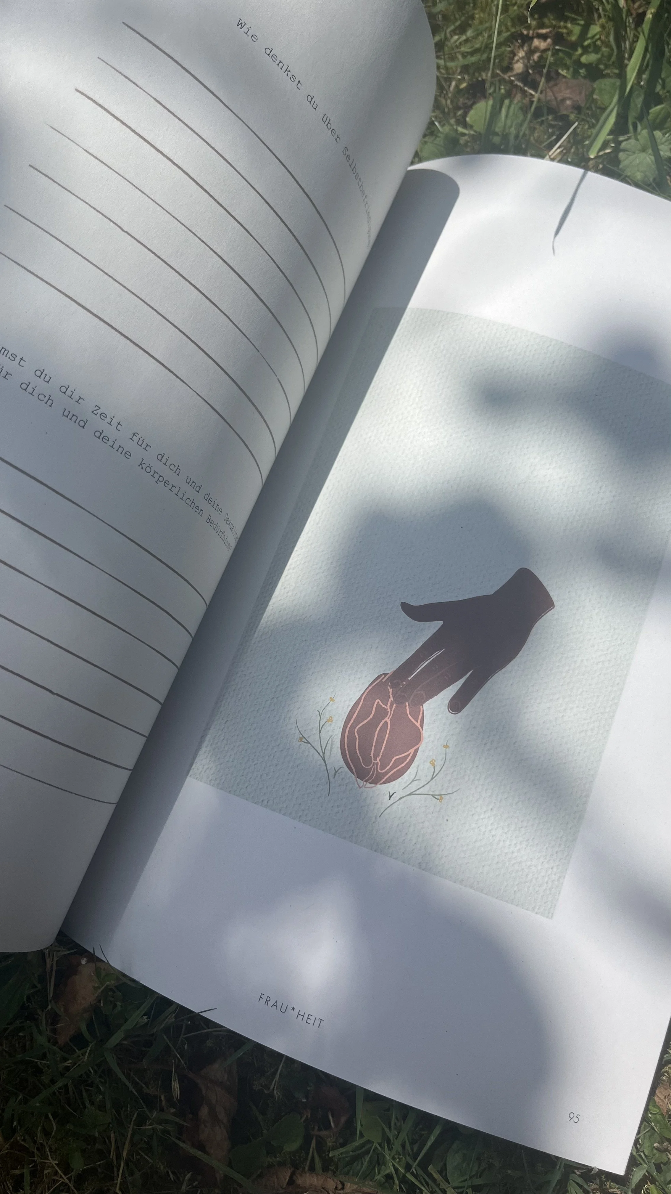 Open book outdoors with a page featuring an illustration of a hand holding a brain, surrounded by delicate plant illustrations. The book appears to be in German.
