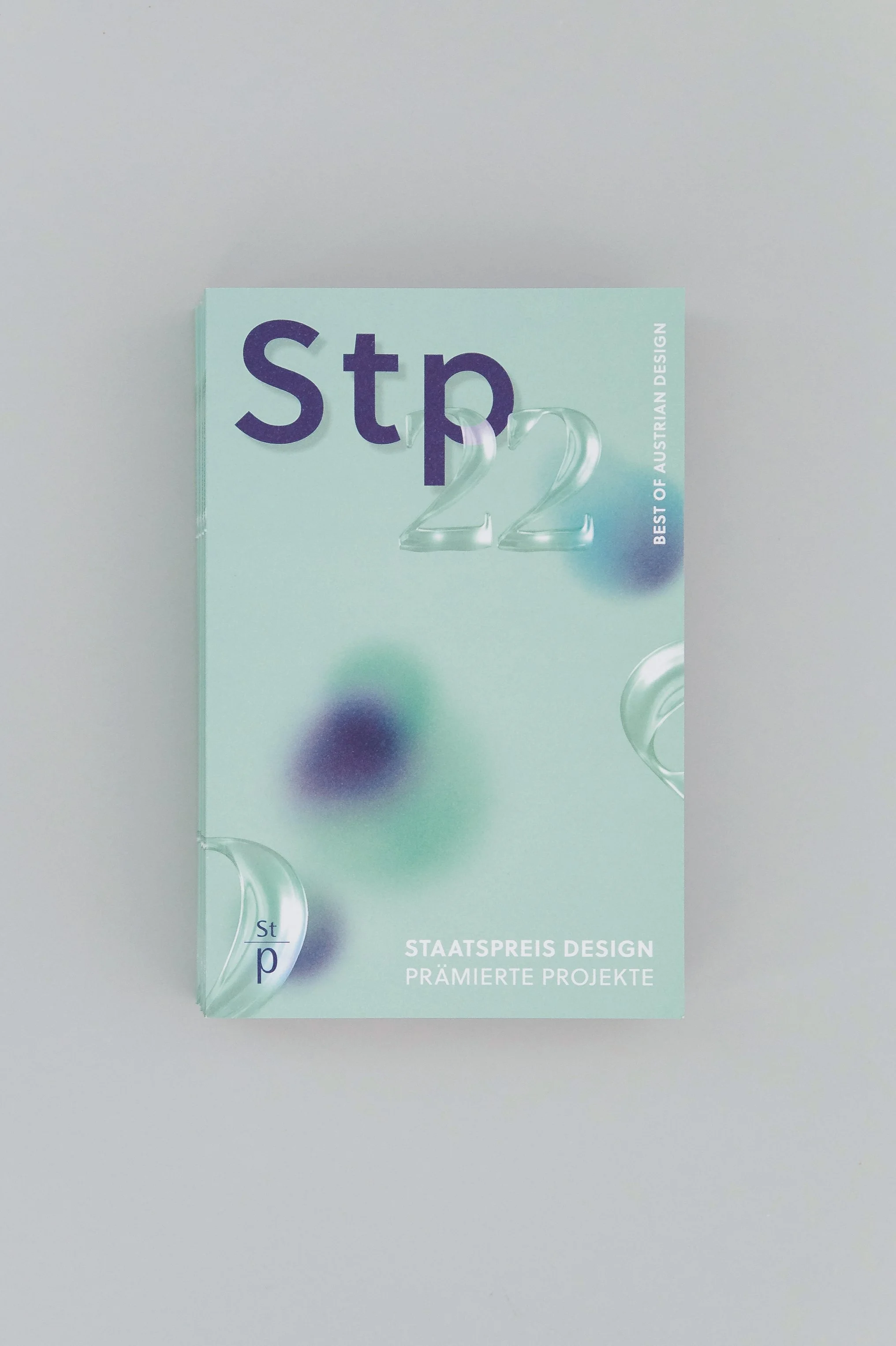 Buchcover des Preises 'Staatspreis Design' mit blauer und grüner Farbgestaltung, großen Ziffern '22' und schönen transparenten Design-Elementen.