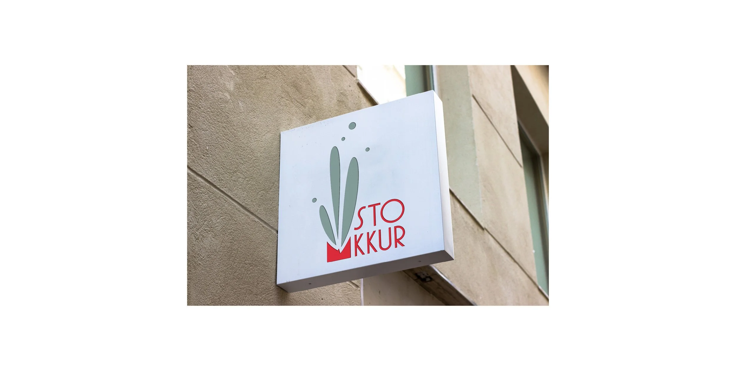 Ein graues Schild an einer Gebäudewand mit einem stilisierten Pflanzenmotiv und der Aufschrift "STOP KUR" in roten Buchstaben.