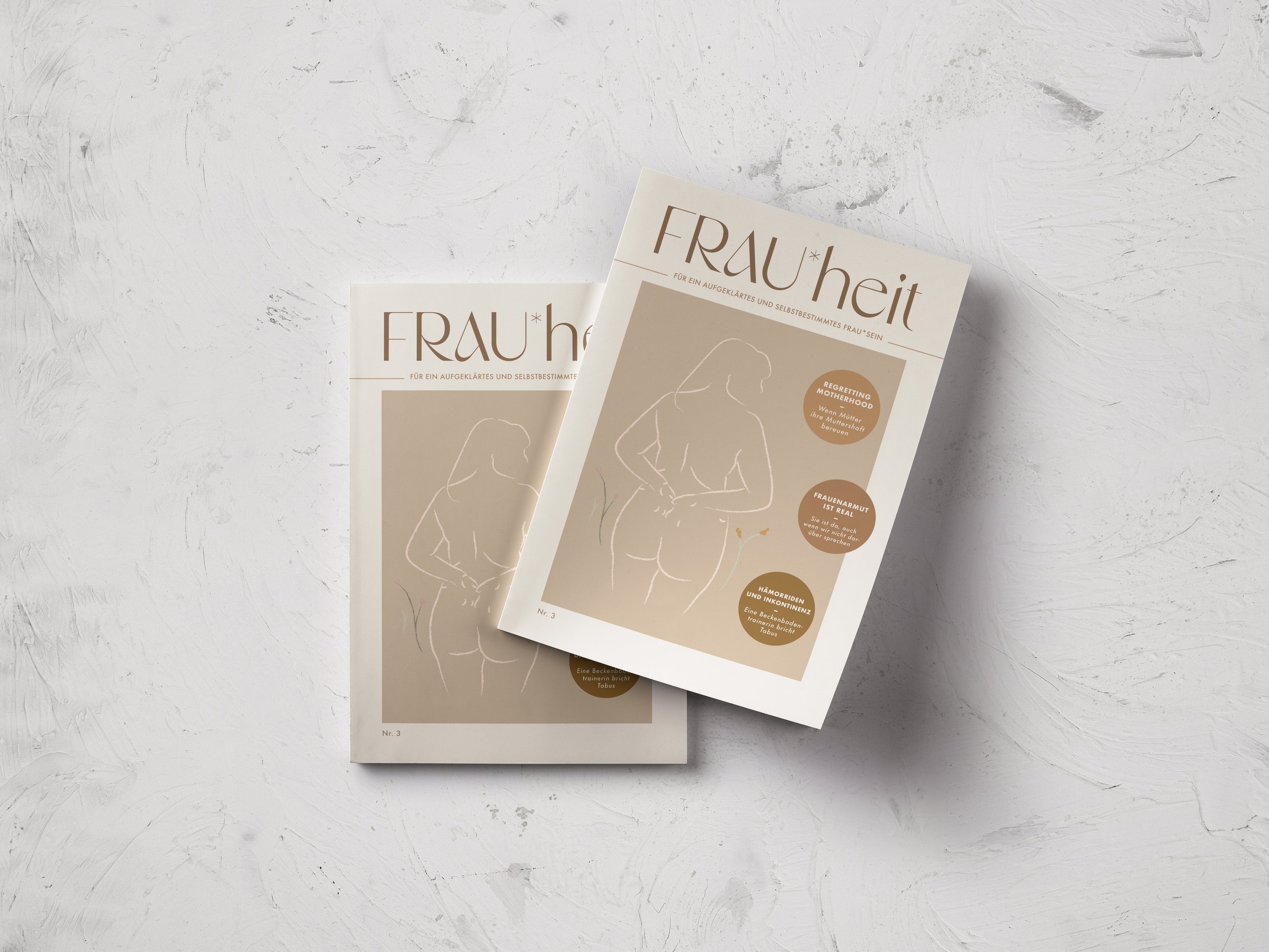 Two magazines titled 'FRAU*heit' with minimalist line art of a woman on the cover, placed on a white textured surface.