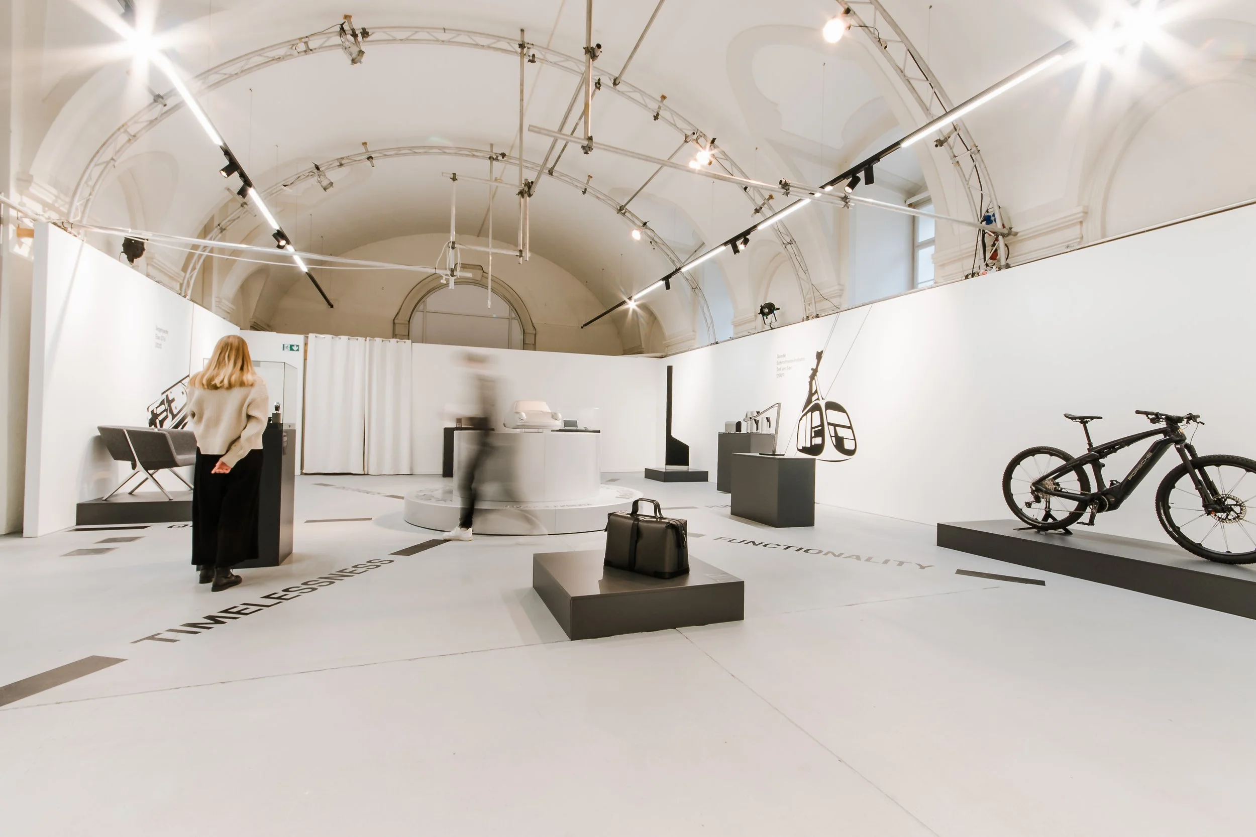 Ausstellung mit Fahrrädern, Skiern und Museumskunst in einem hellen Raum mit hohen Decken, weißen Wänden und Lichtinstallationen.
