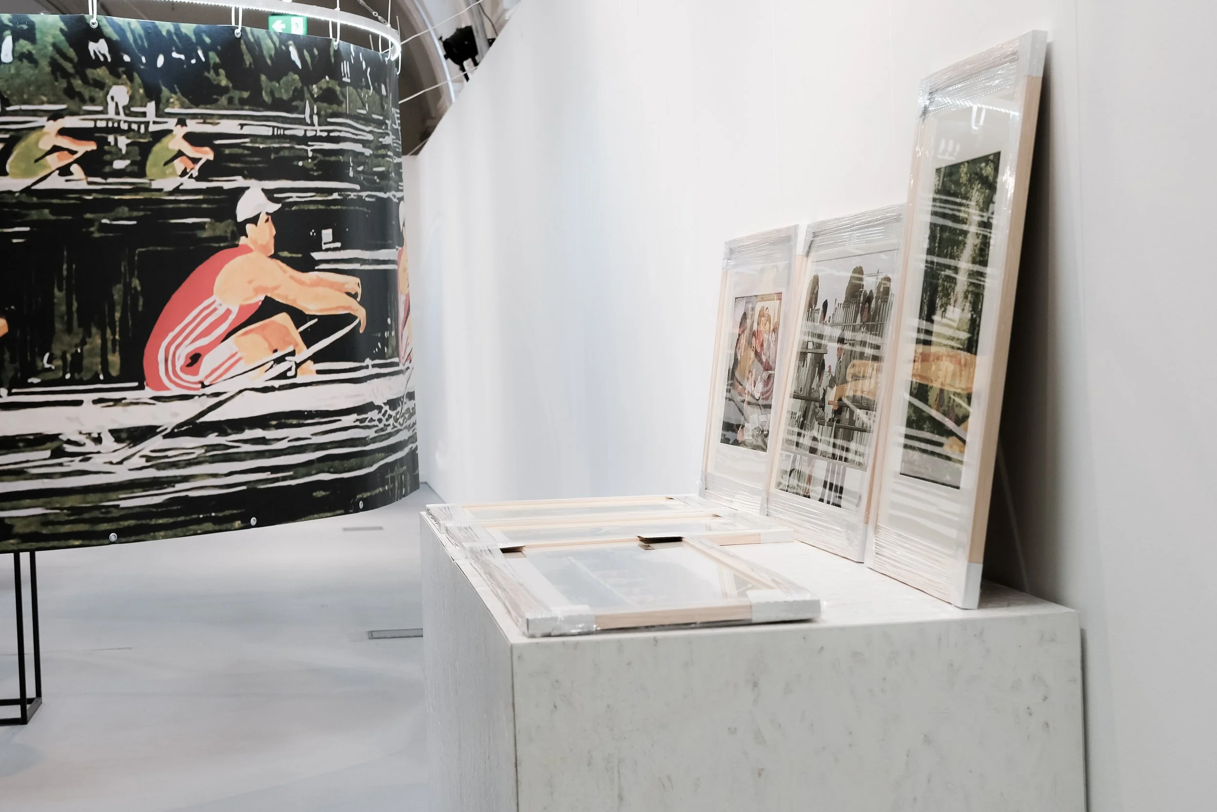 Ausstellung mit aufgestellten Bildern in Rahmen und eine große, schwarze Leinwand mit sportlichen Figuren beim Laufen.