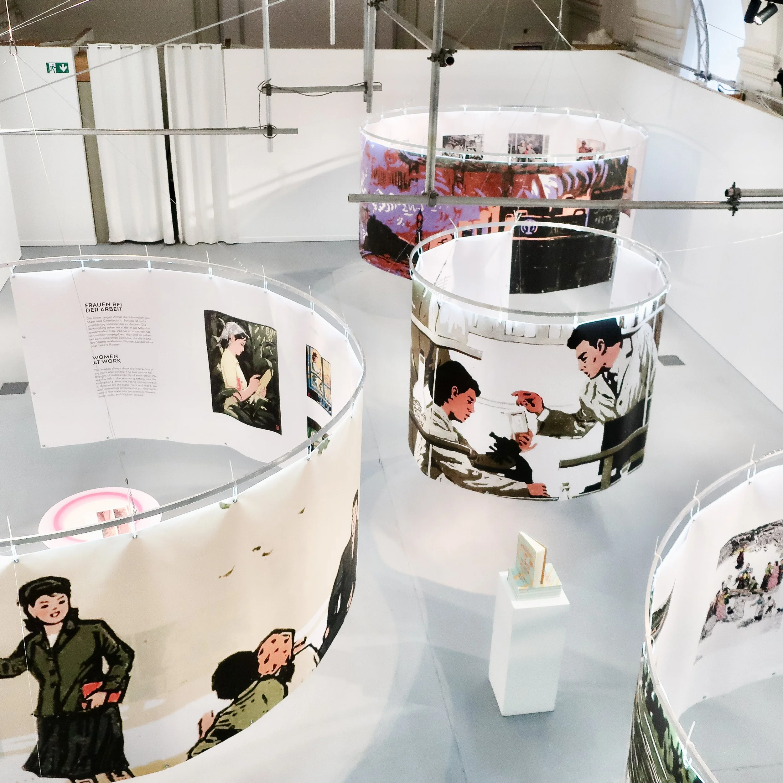 Ausstellung mit mehreren Frontalansichten von Frauen bei der Arbeit, die auf weißen Trennwänden hängen.