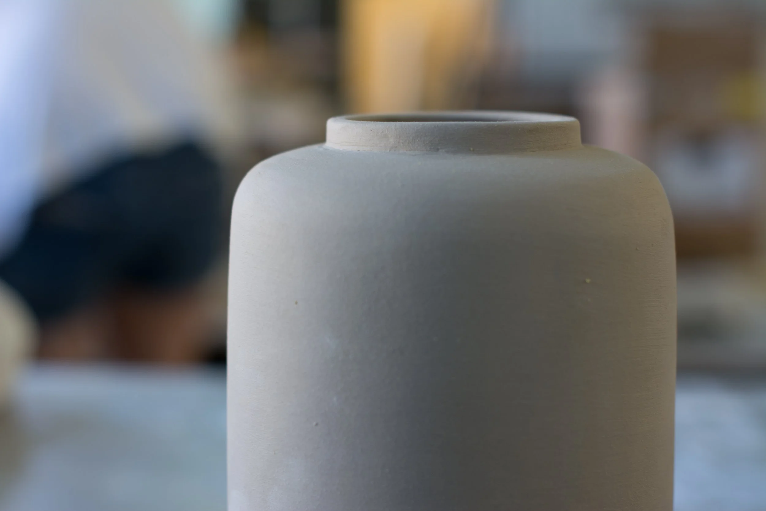 Nahaufnahme einer leeren, weißen Keramikvase mit weitem Hals auf einem Tisch, unscharfer Hintergrund.