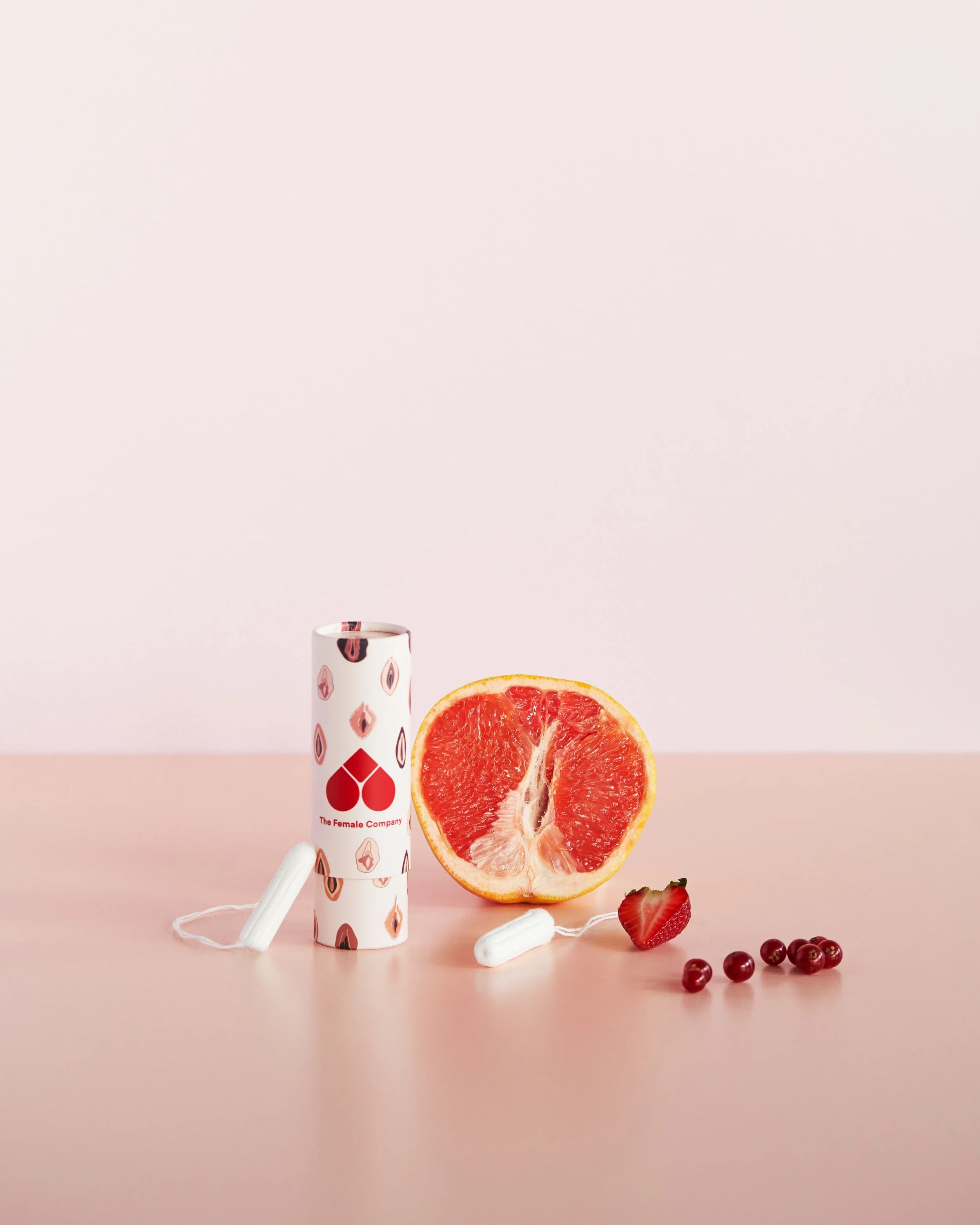 Ein Glas mit Sticker, eine Grapefruit, Erdbeeren, schwarze Johannisbeeren, ein weißer Gegenstand, eine Kordel, eine Kerze, eine Strawberry Clay Mask, eine zerschnittene Grapefruit, eine Spitze, ein Reagenzglas mit Schlagsahne, eine rosa Oberfläche und ein heller Hintergrund.