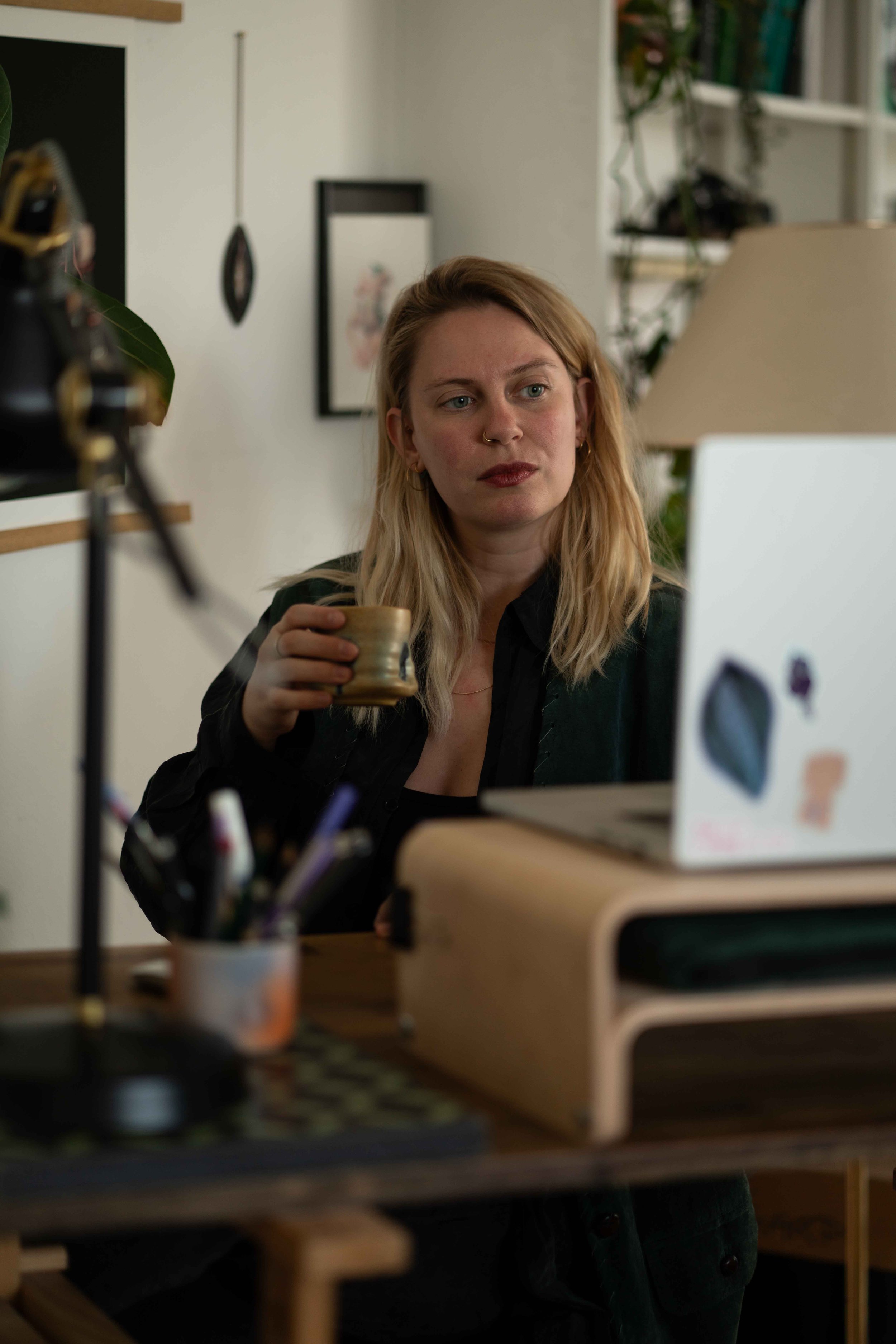 Eine Frau mit langem blonden Haar, die in einem Büro an einem Laptop arbeitet und eine Tasse hält.