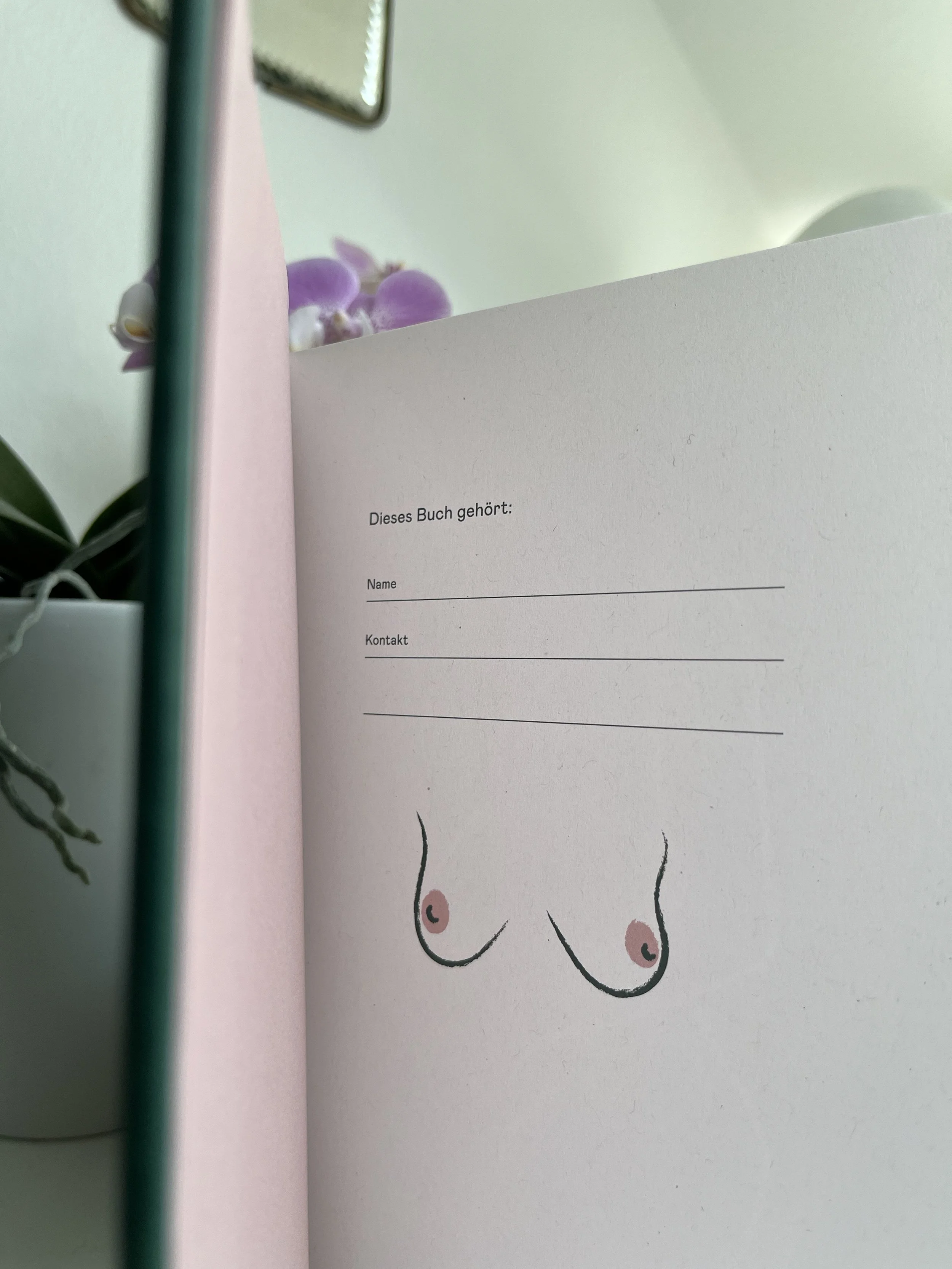 In diesem Bild sieht man einen geöffneten Bogen mit einem Text in Deutsch, der lautet: "Dieses Buch gehört" gefolgt von Linien für den Namen und Kontaktinformationen. Im Hintergrund sind pinke Orchideen und eine umgedrehte Briefmarke zu sehen.
