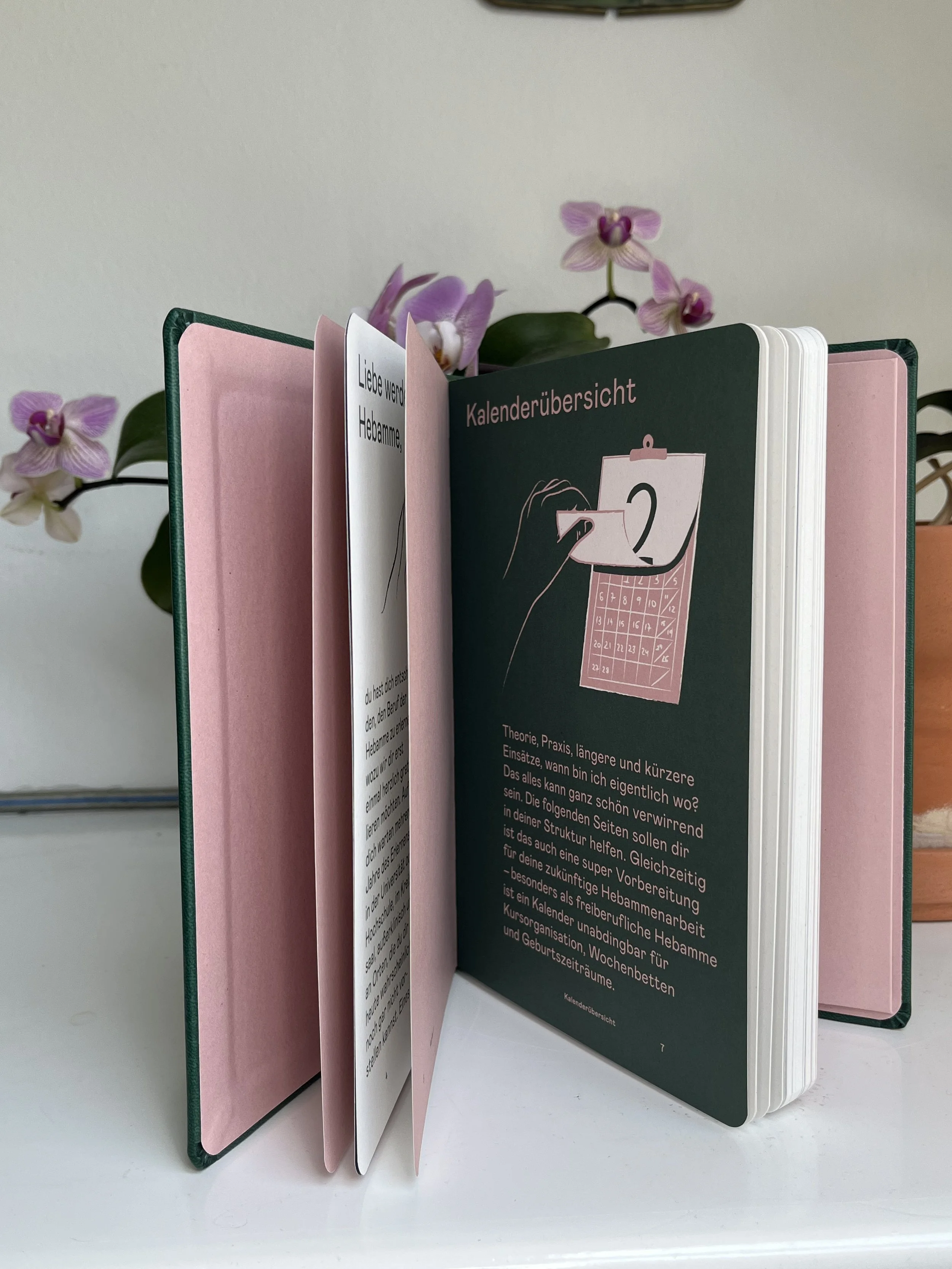 Ein Organizer mit verschiedenen Seiten, darunter eine mit Kalenderübersicht und Text in deutscher Sprache, daneben eine Orchidee im Hintergrund.