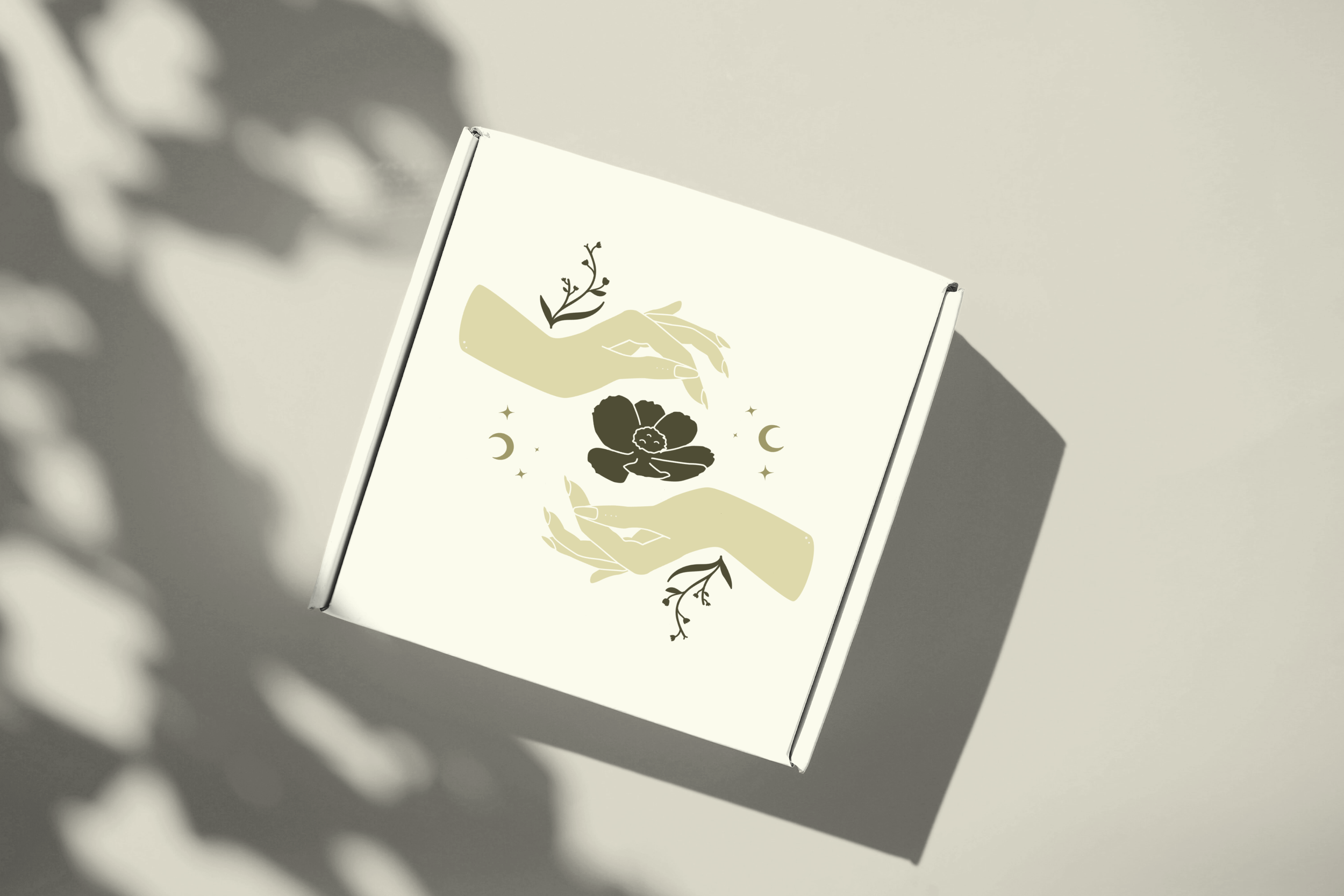 Einふweißes Pappkarton mit einer stilisierten Illustration von zwei Händen, die eine Blume zwischen sich halten, umgeben von kleinen Sternen, Monden und Blättern.